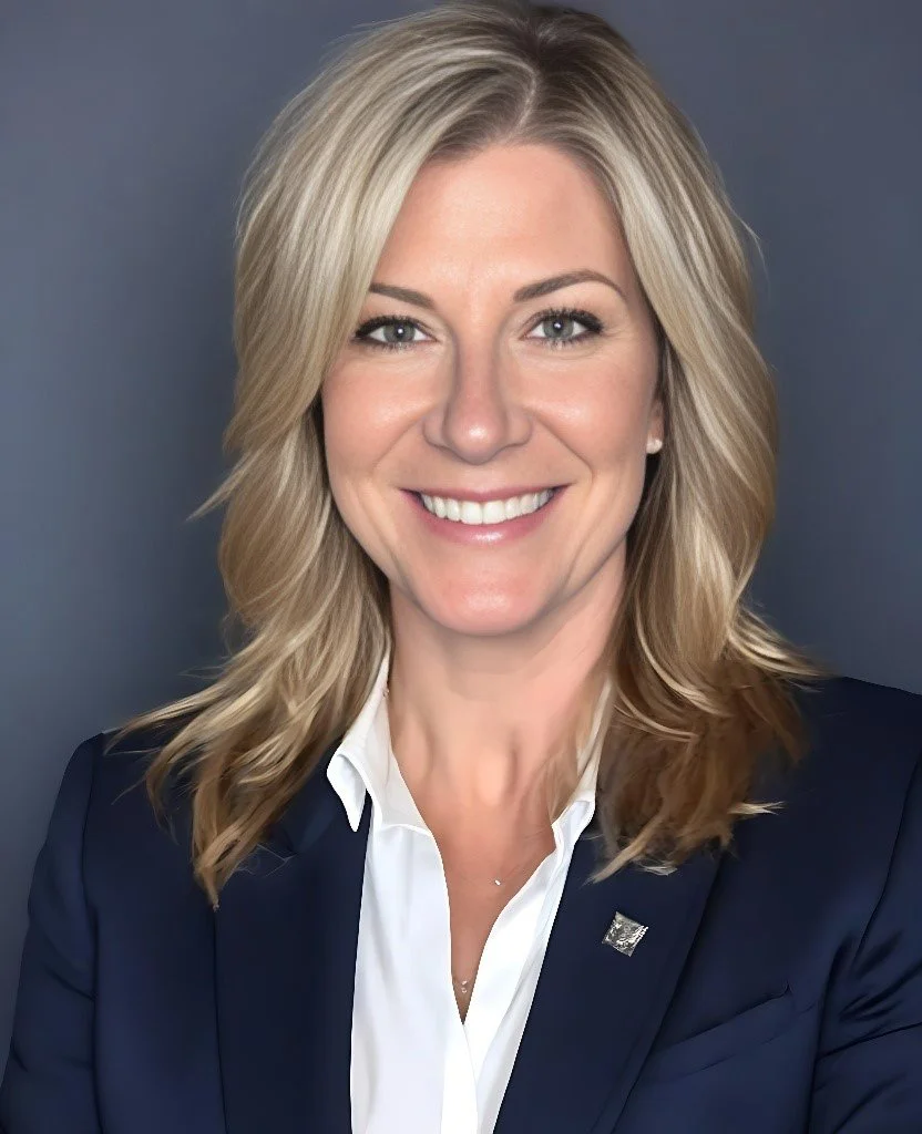 Professional woman with shoulder-length blonde hair, wearing a navy blazer and white blouse, smiling against a gray background.