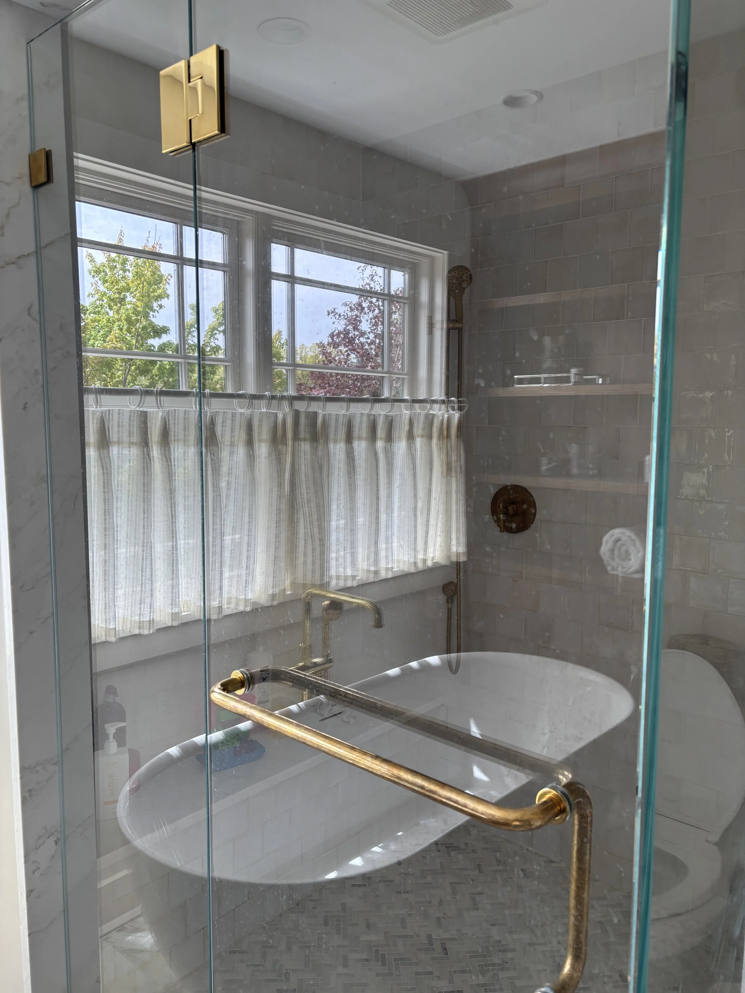 A bathroom shower with large window, striped curtain, and brass grab bar.