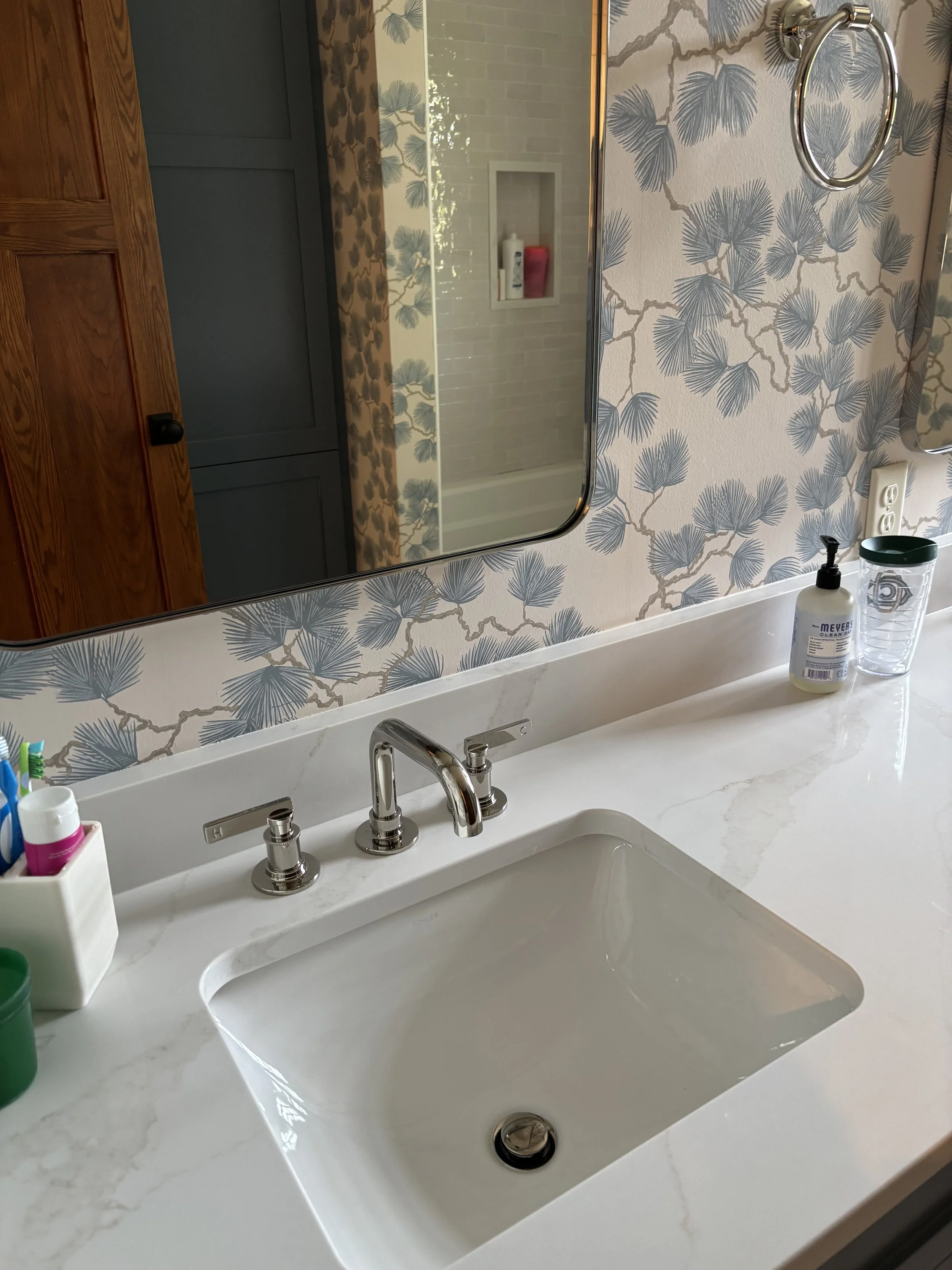 A bathroom sink with a white marble countertop, a rectangular undermount sink, and a chrome faucet. To the left of the sink, there is a white cup holding toothbrushes and toothpaste. To the right of the sink, there is a bottle of hand soap with a pum