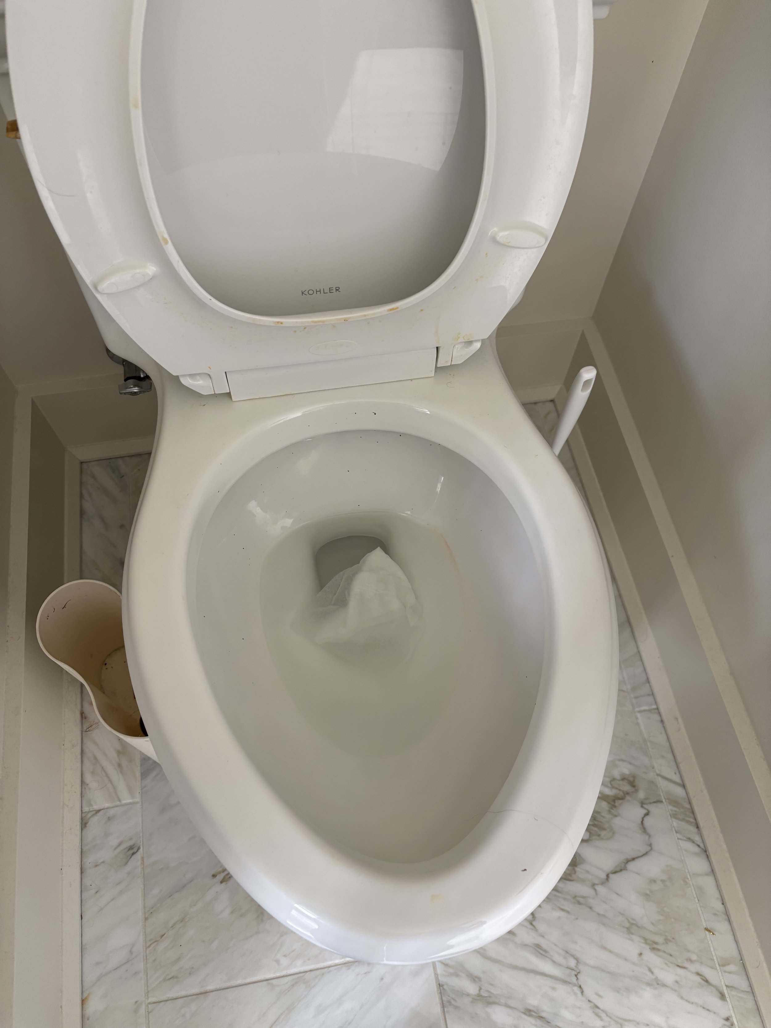 Toilet with its lid open, located in a bathroom with marble flooring, next to a small trash bin.