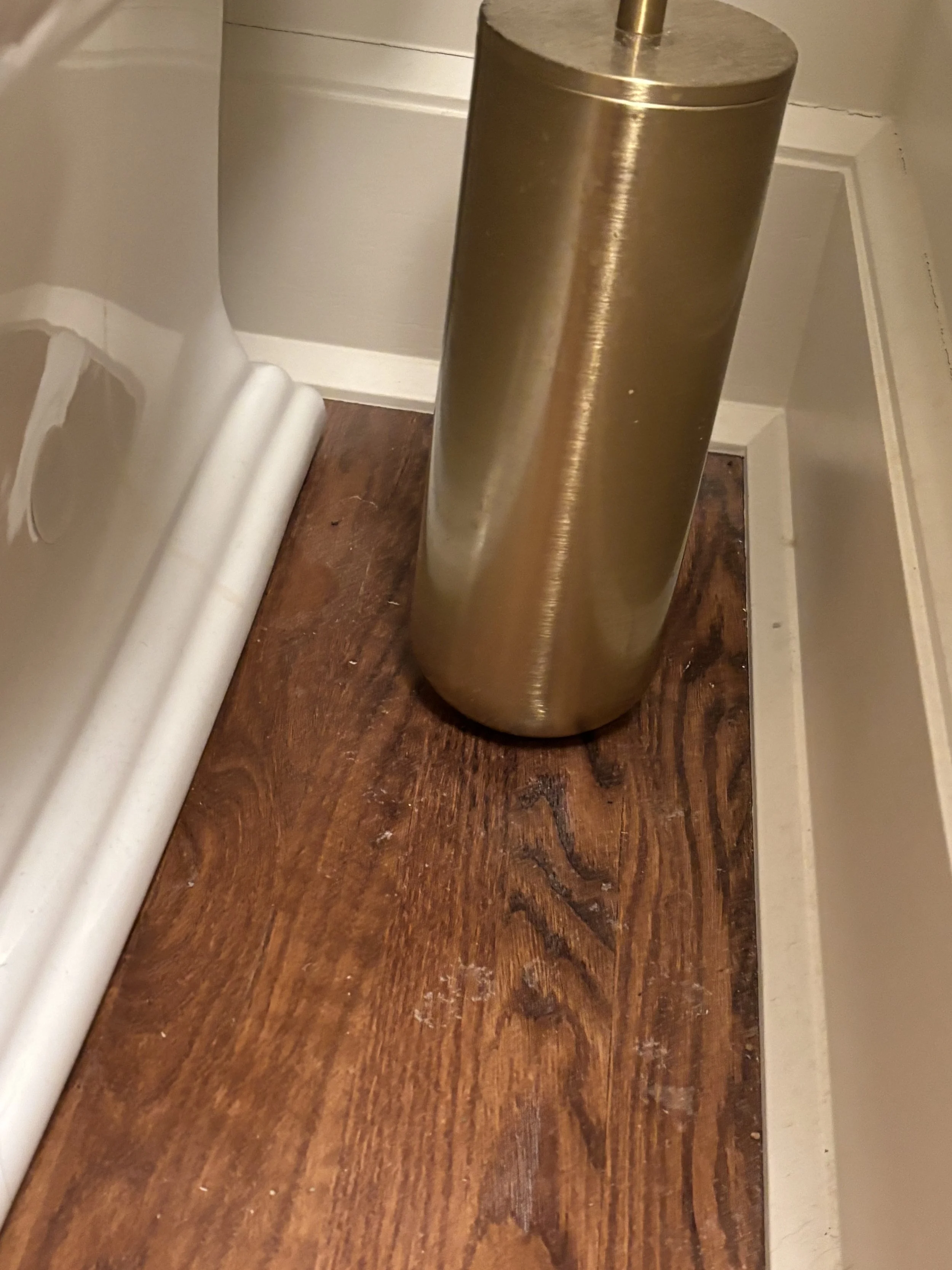A close-up of a metallic paper towel holder on a wooden countertop in a bathroom or kitchen, with part of a white wall and some molding visible.