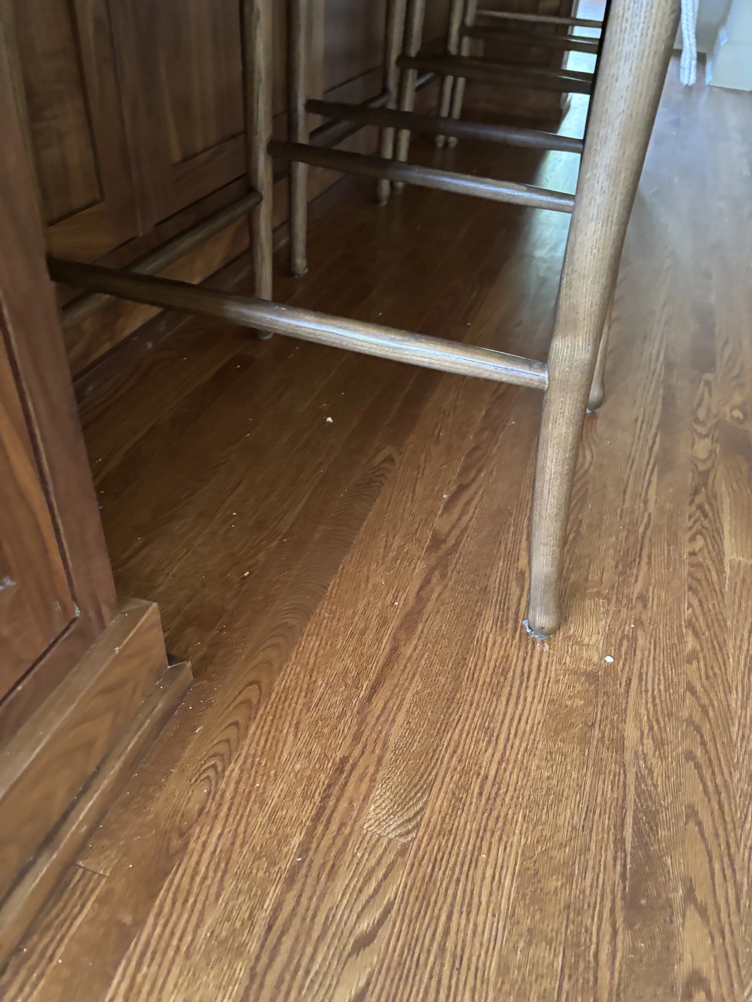 The image shows a room with wooden flooring and wooden furniture, likely the bottom part of a table or chair. The furniture appears to be made of medium-toned wood with a polished finish. Part of a wooden staircase is visible in the background. There