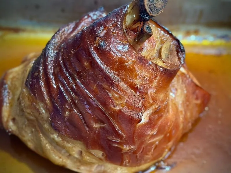 Close-up of a cooked pork knuckle wrapped with bacon, resting on a cooking surface.
