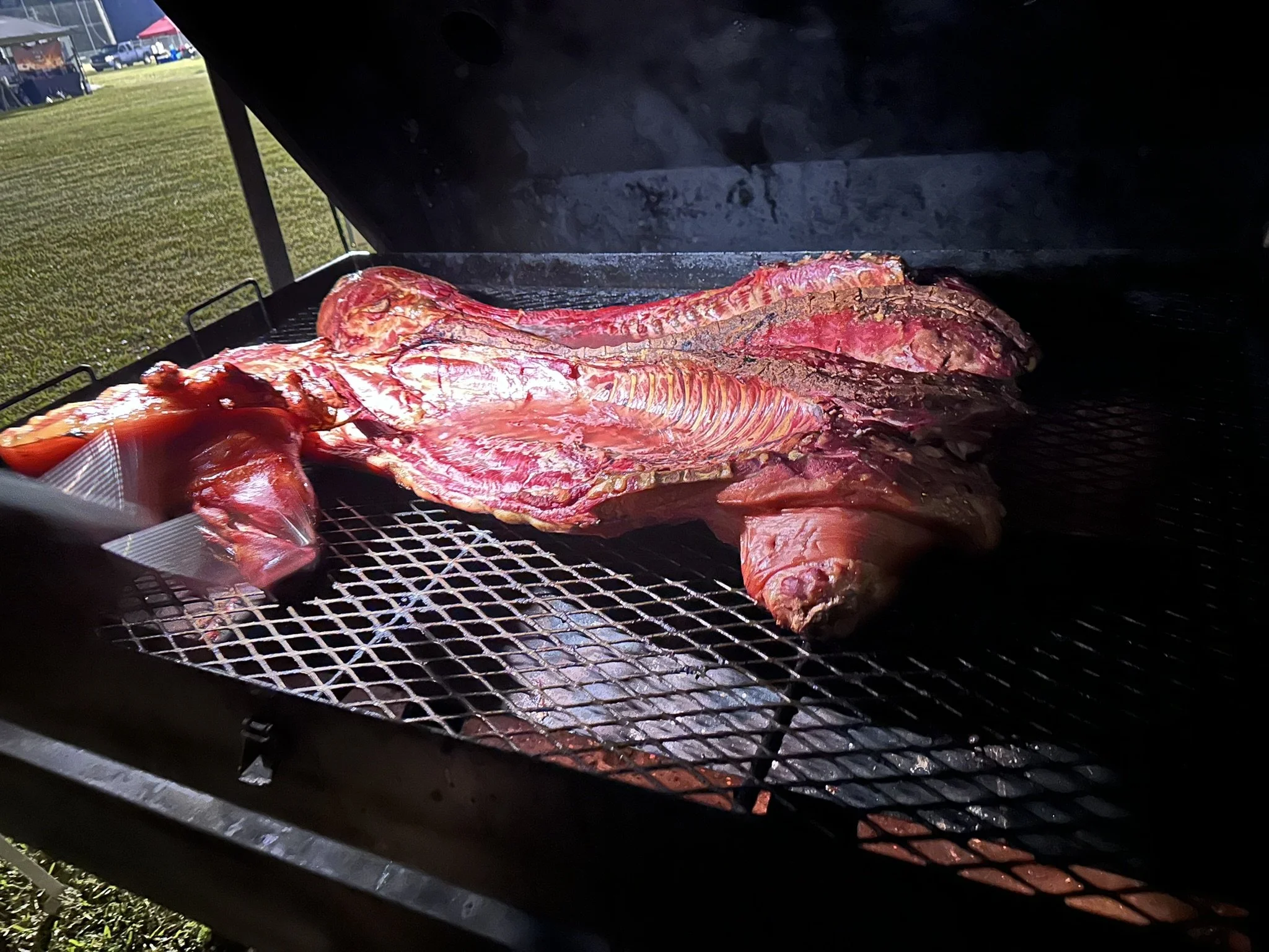 Meat being cooked on a grill outside during daytime.