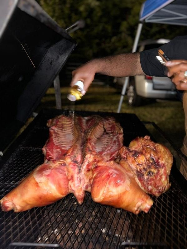 Person seasoning large cuts of meat on a grill outdoors.