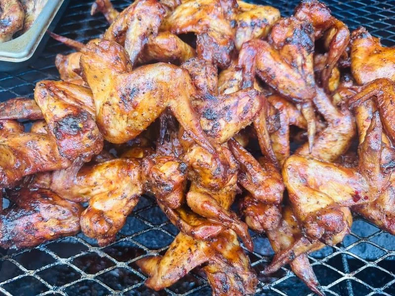 Grilled chicken wings on a wire rack with a side of dipping sauce.