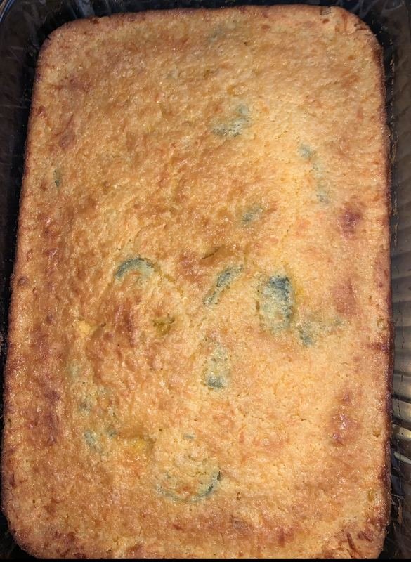A rectangular, cooked dish, possibly a casserole or banana bread, with a golden brown crust and some visible greenish or bluish spots.