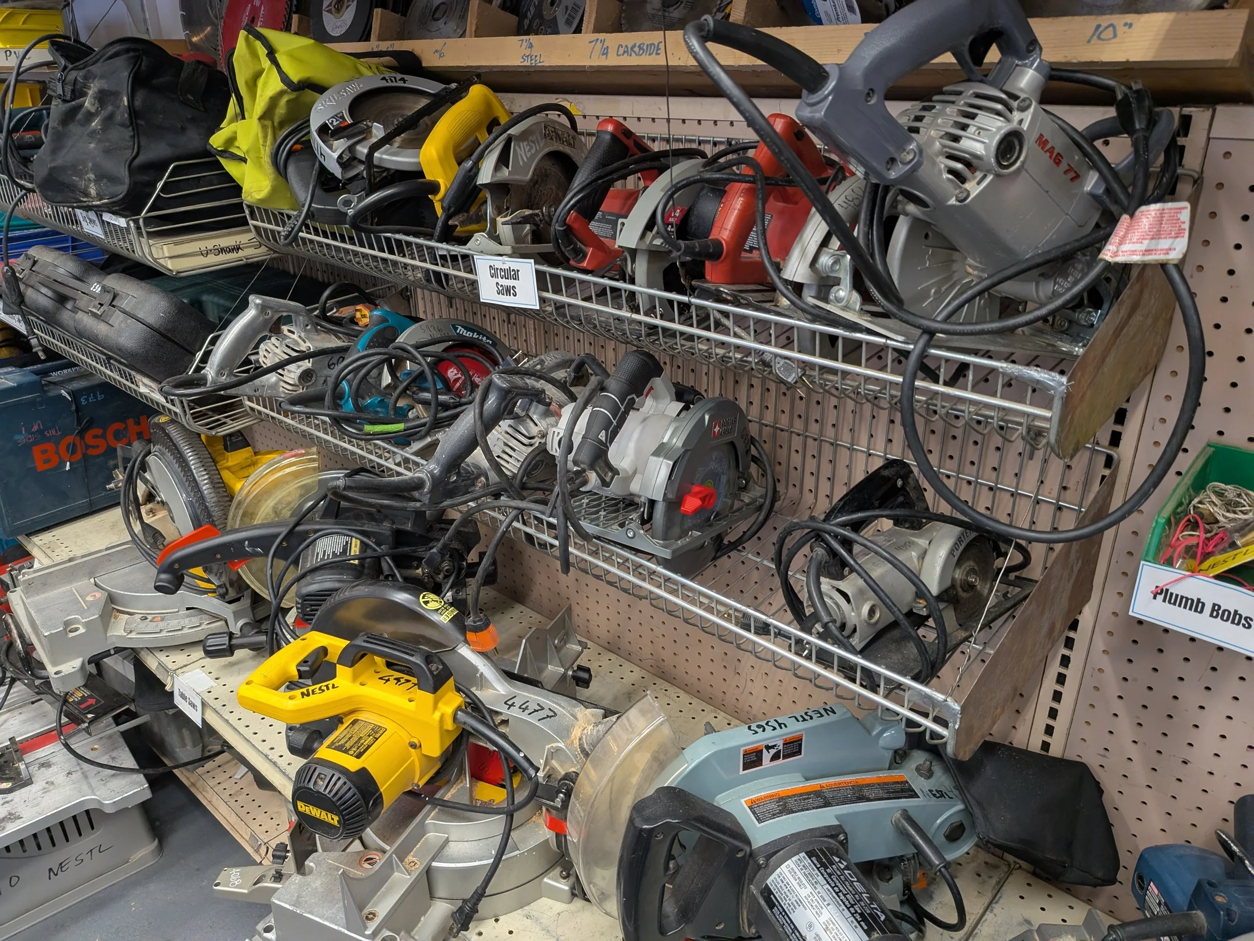 A variety of power tools and equipment on shelves in a hardware store, including circular saws, drills, and other hand tools.
