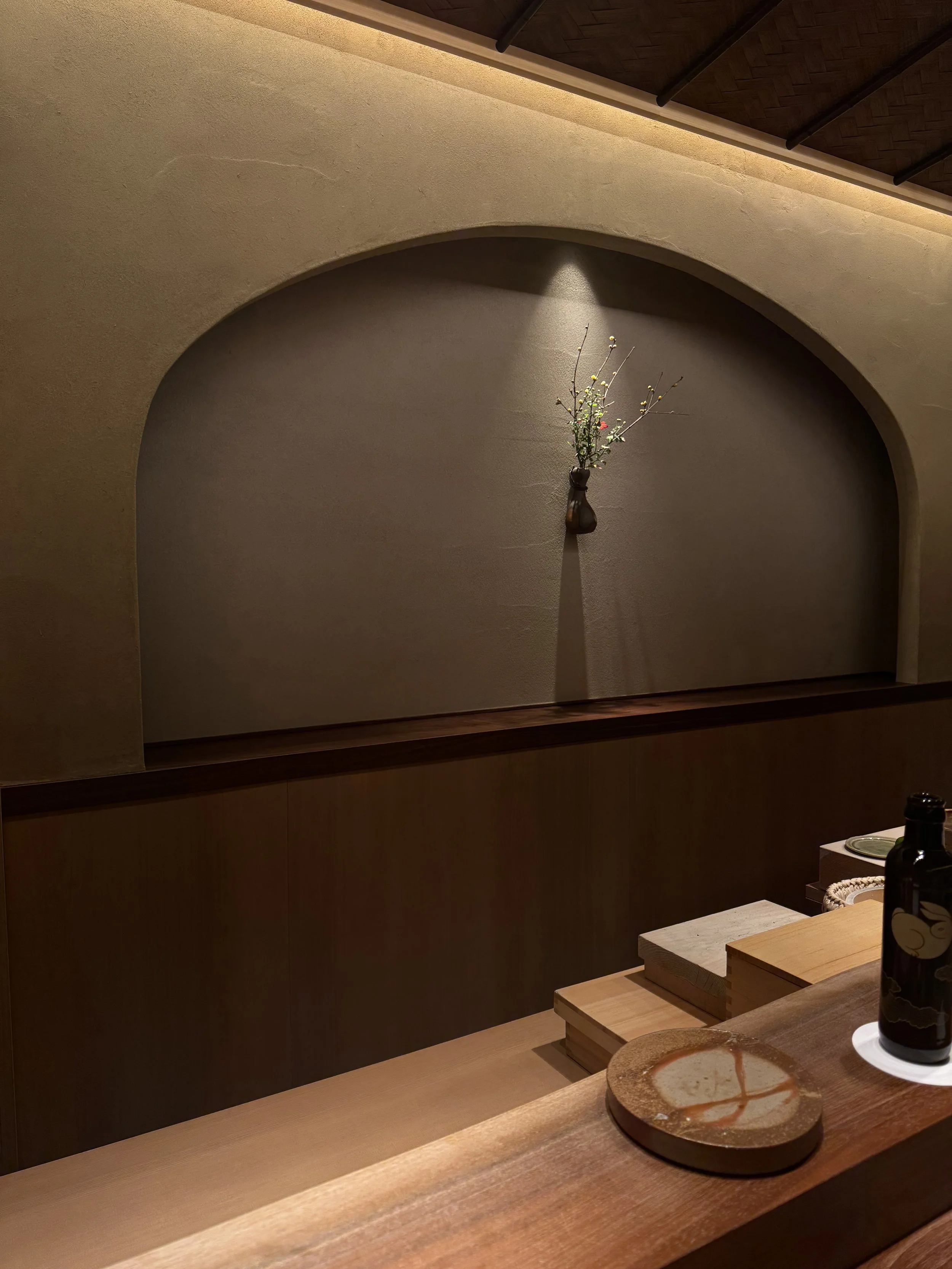 A minimalist interior wall with a small vase of branches and a light shining above.