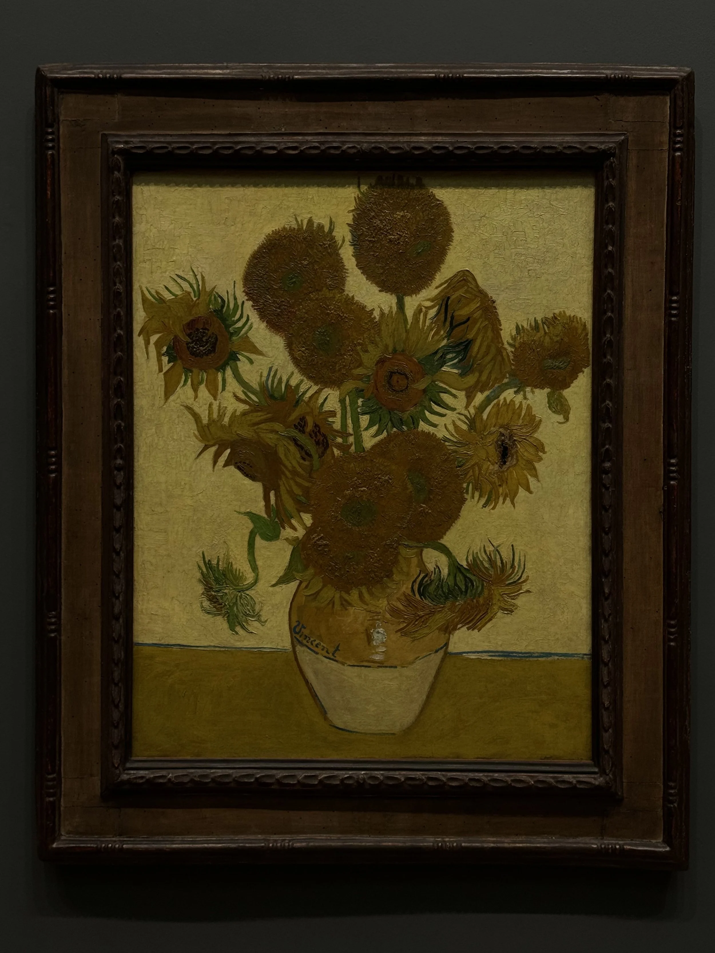 A framed painting of sunflowers in a yellow vase against a warm background.