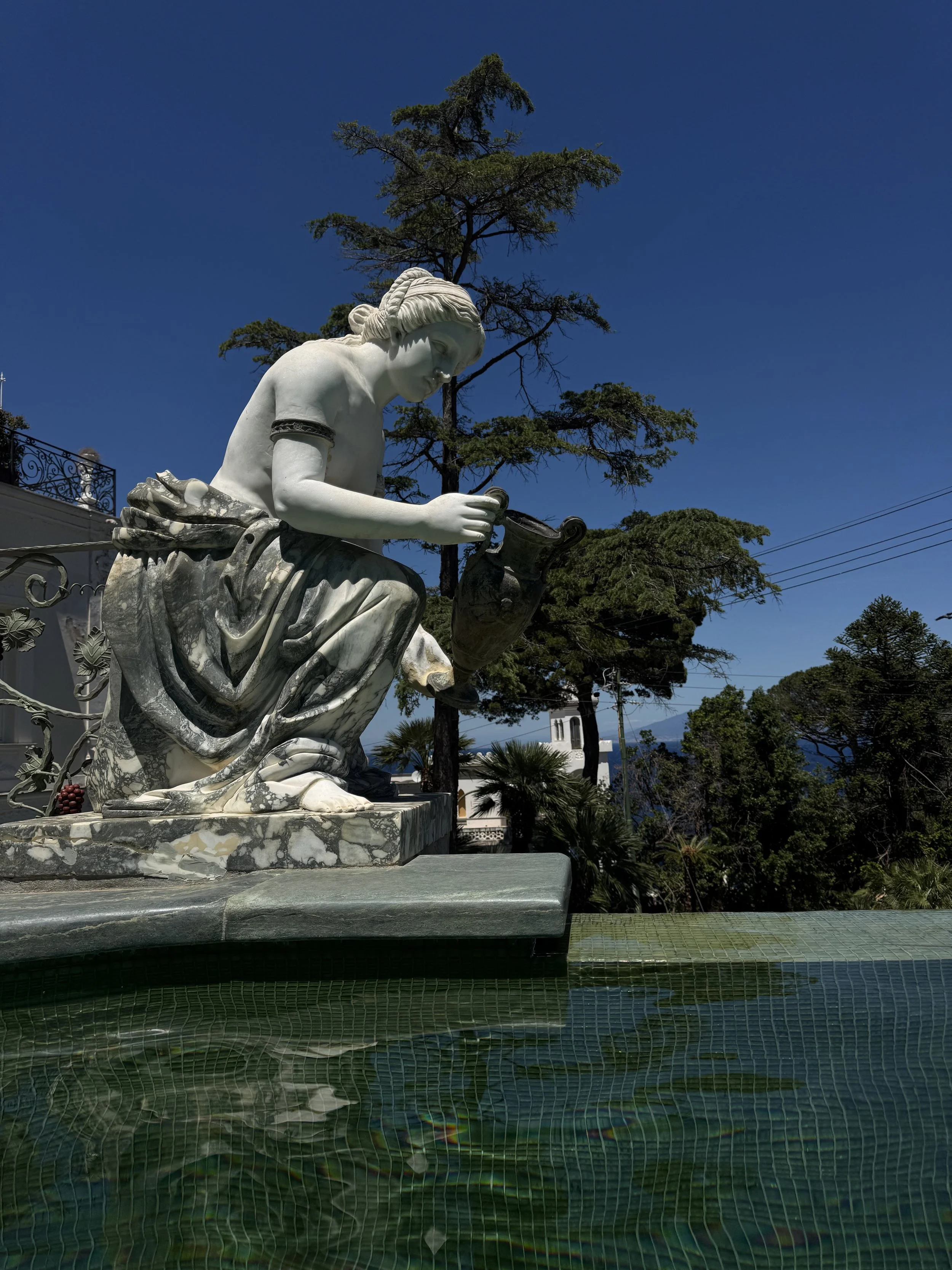 White marble statue of a girl reading a book, with trees and a building in the background.