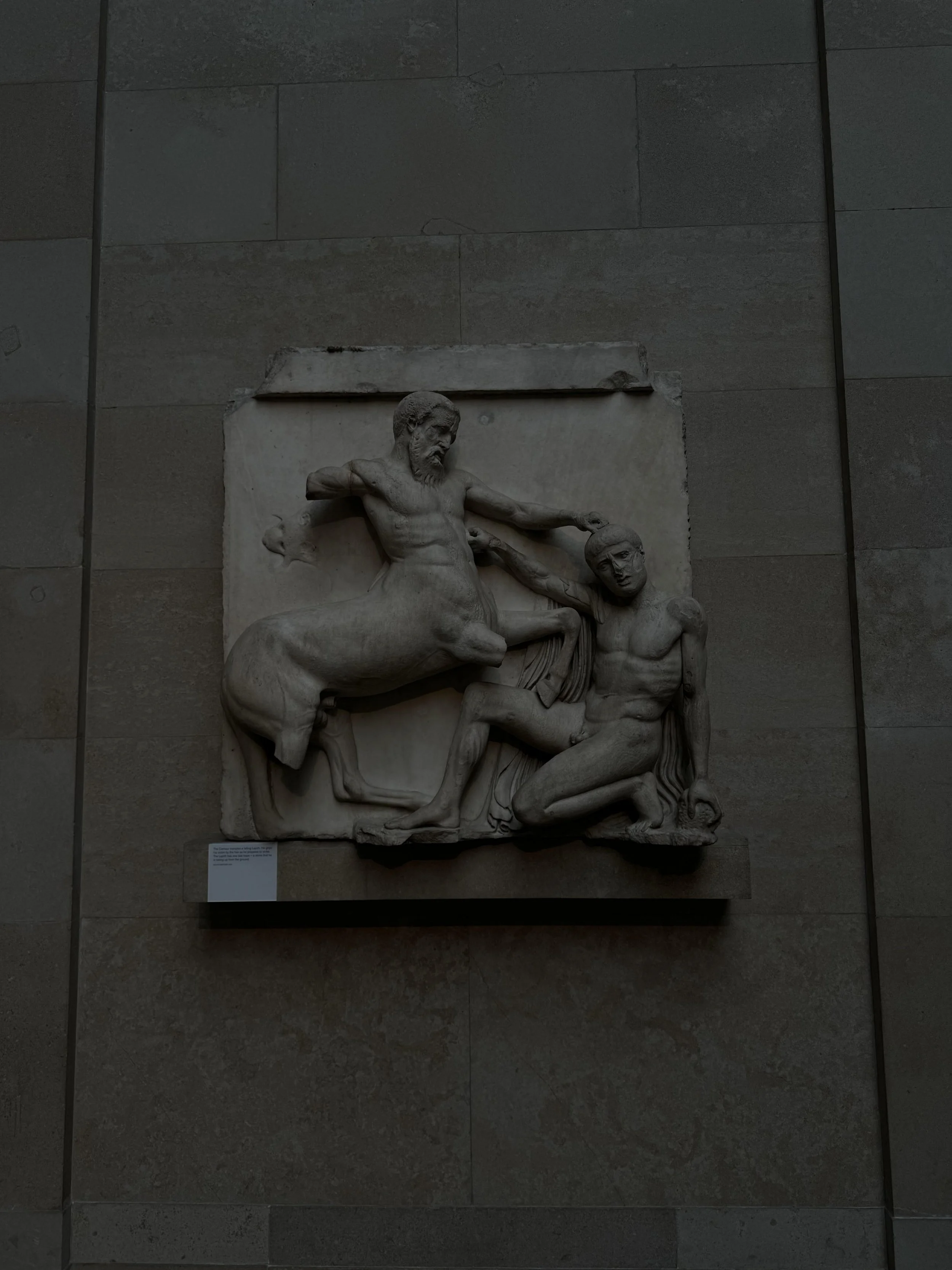 Marble relief sculpture depicting a bearded man grabbing a younger man's head, with both figures partly clothed.