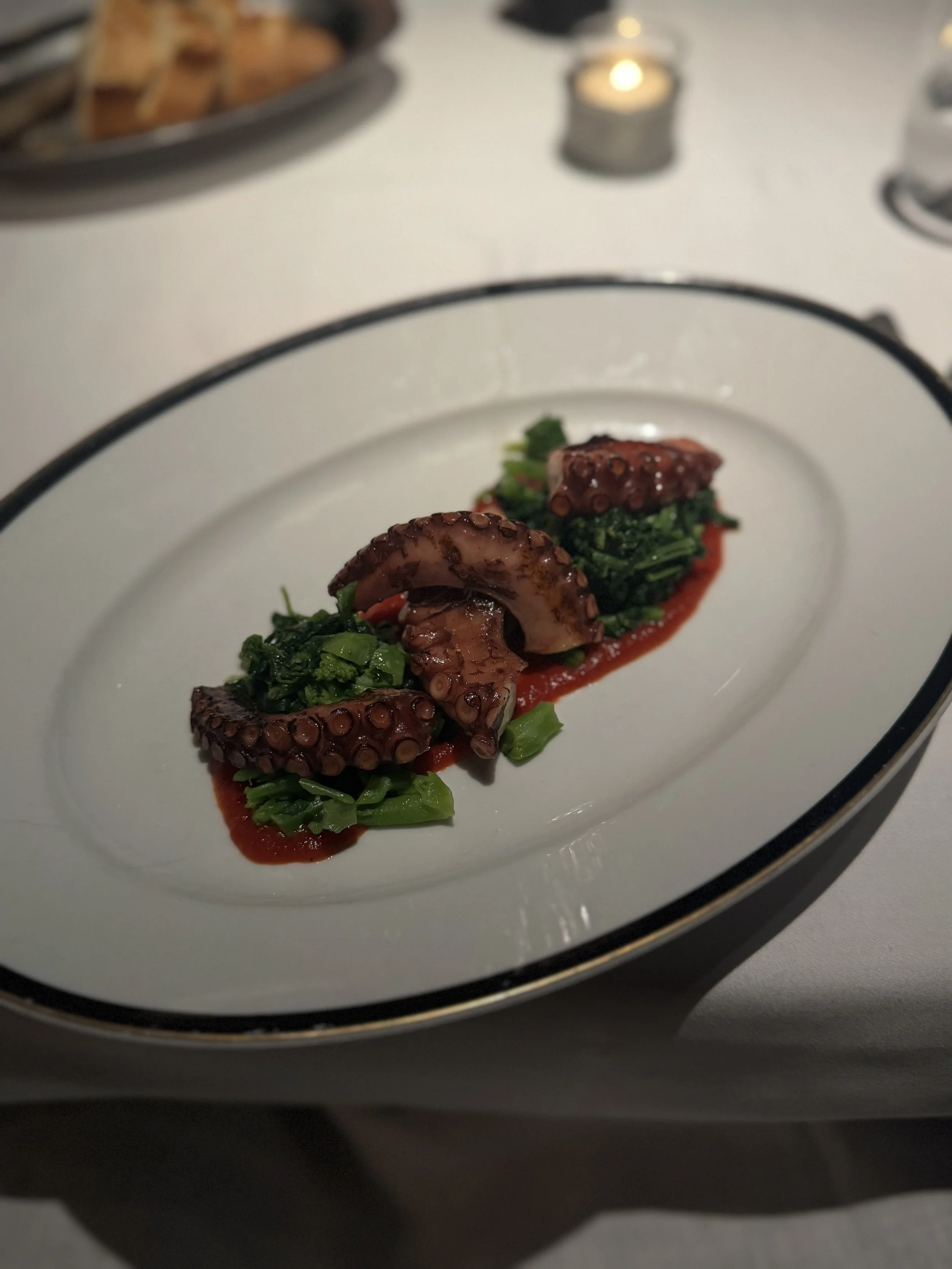 A plate with grilled octopus tentacles on a bed of green vegetables, garnished with red sauce.
