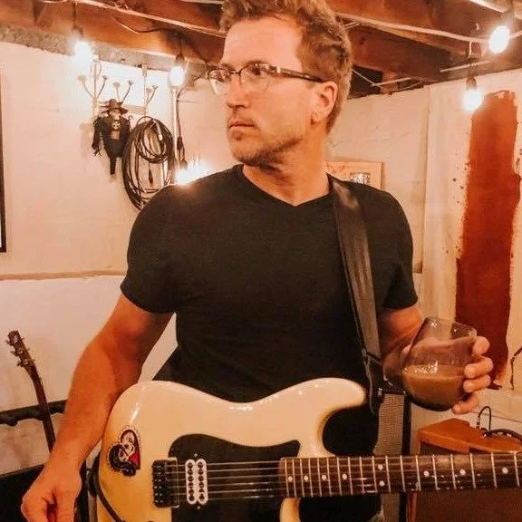 Matt standing in a mood-lit room with an electric guitar