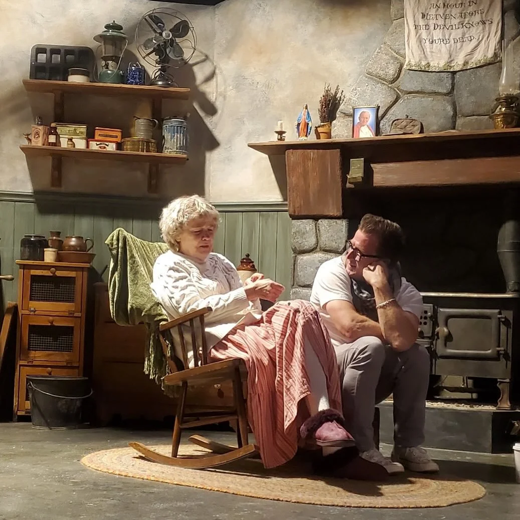 Matt sits on a fireplace next to a woman in a rocking chair