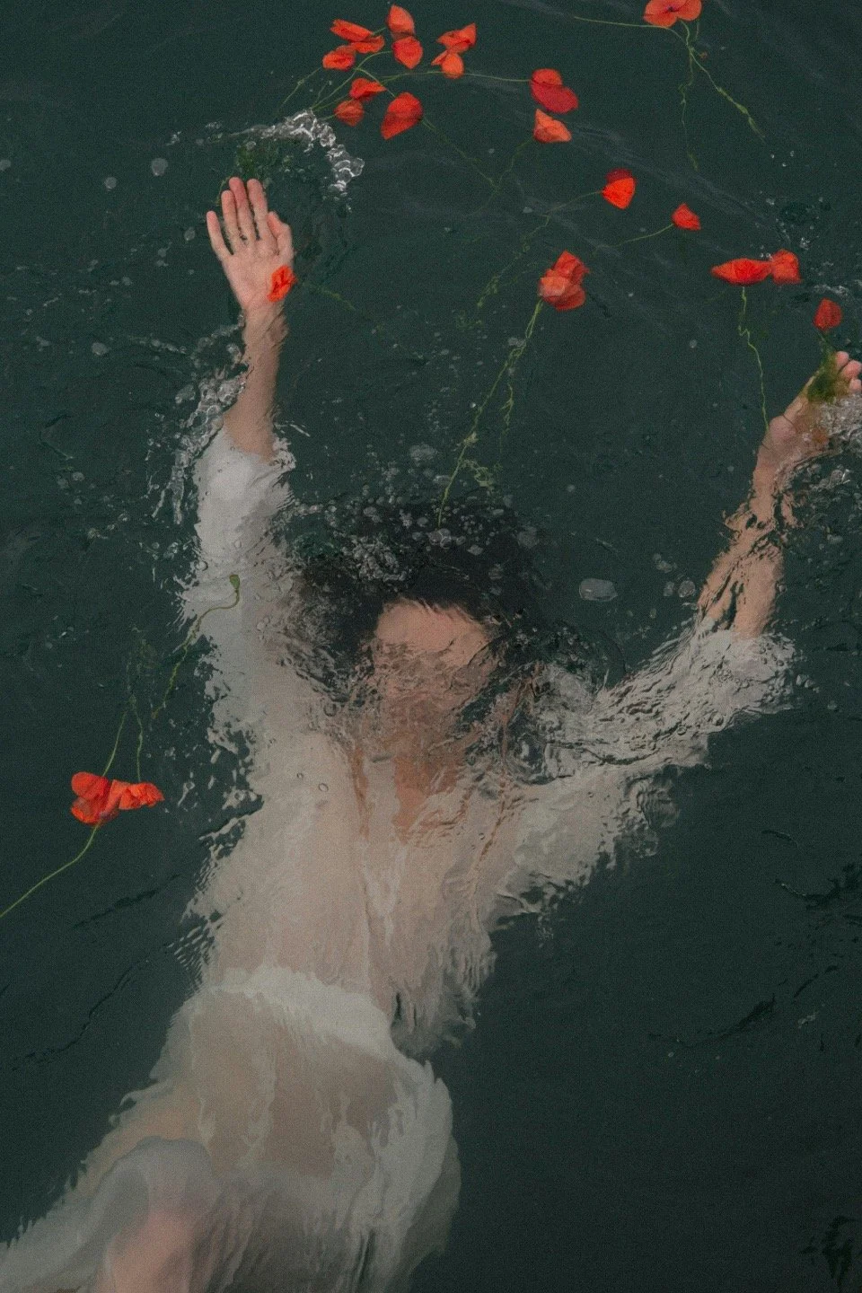 A person swimming underwater with orange flowers floating on the water's surface.