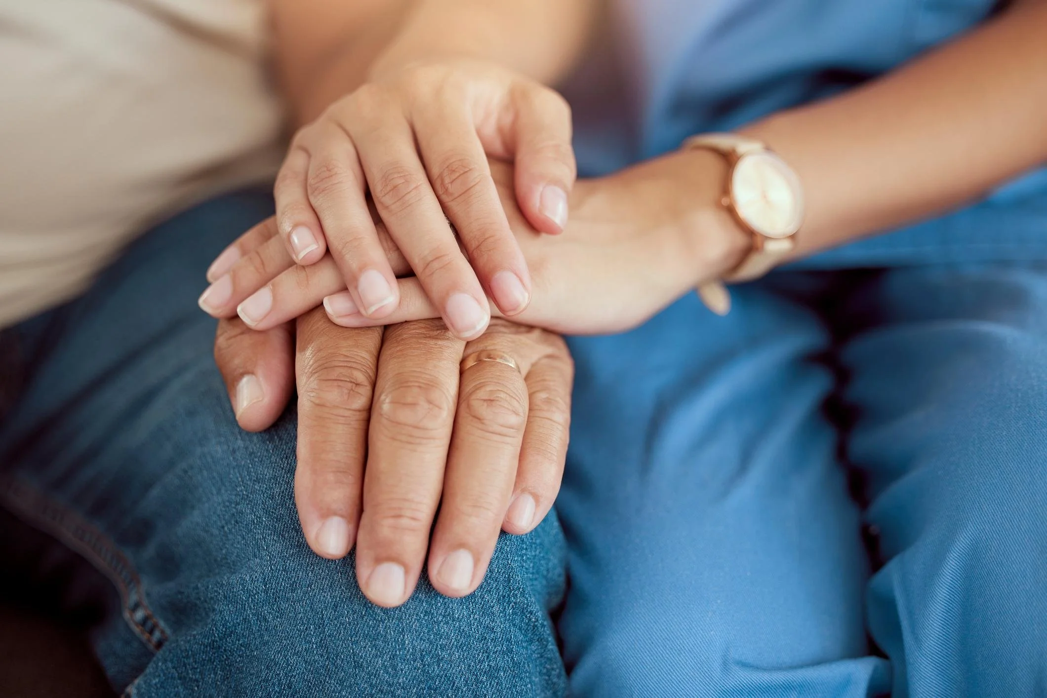 Close-up of a person holding hands with another person, showing the back of a wristwatch and part of a blue shirt.