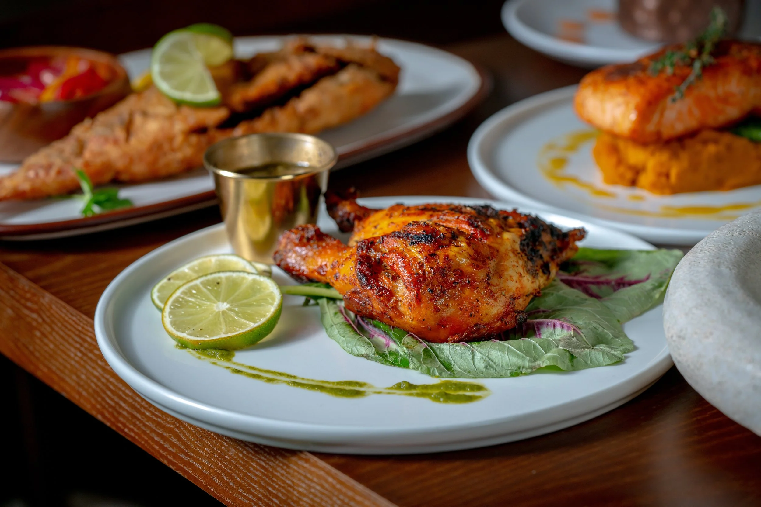 Plate with grilled chicken thigh garnished with lime slices, and other Caribbean dishes in the background.