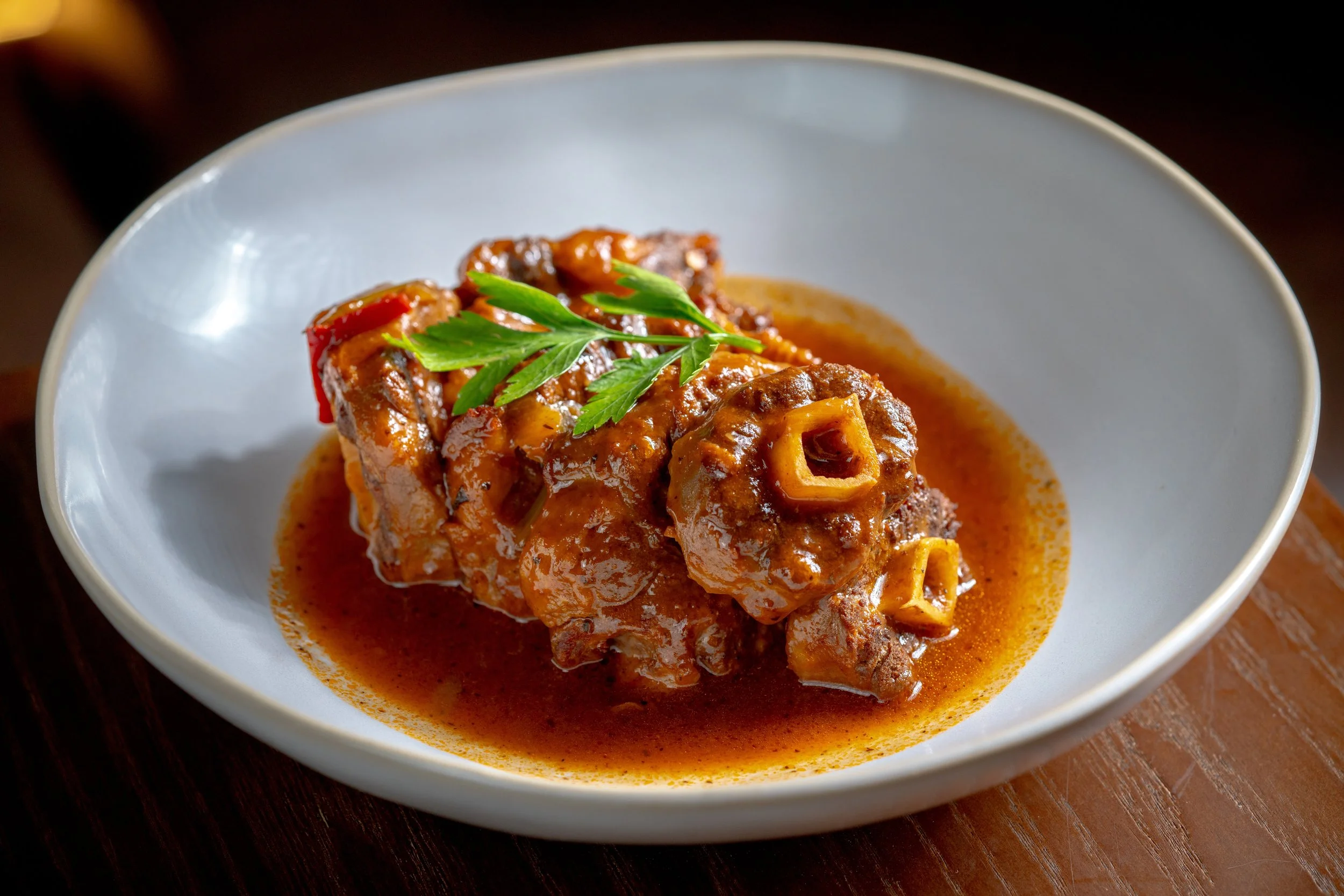 A bowl of beef stew garnished with a sprig of parsley