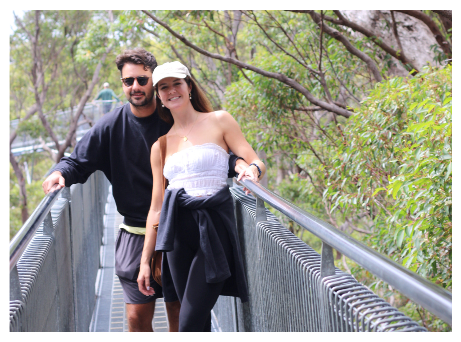 A man and woman standing on an outdoor walkway surrounded by greenery, smiling at the camera.