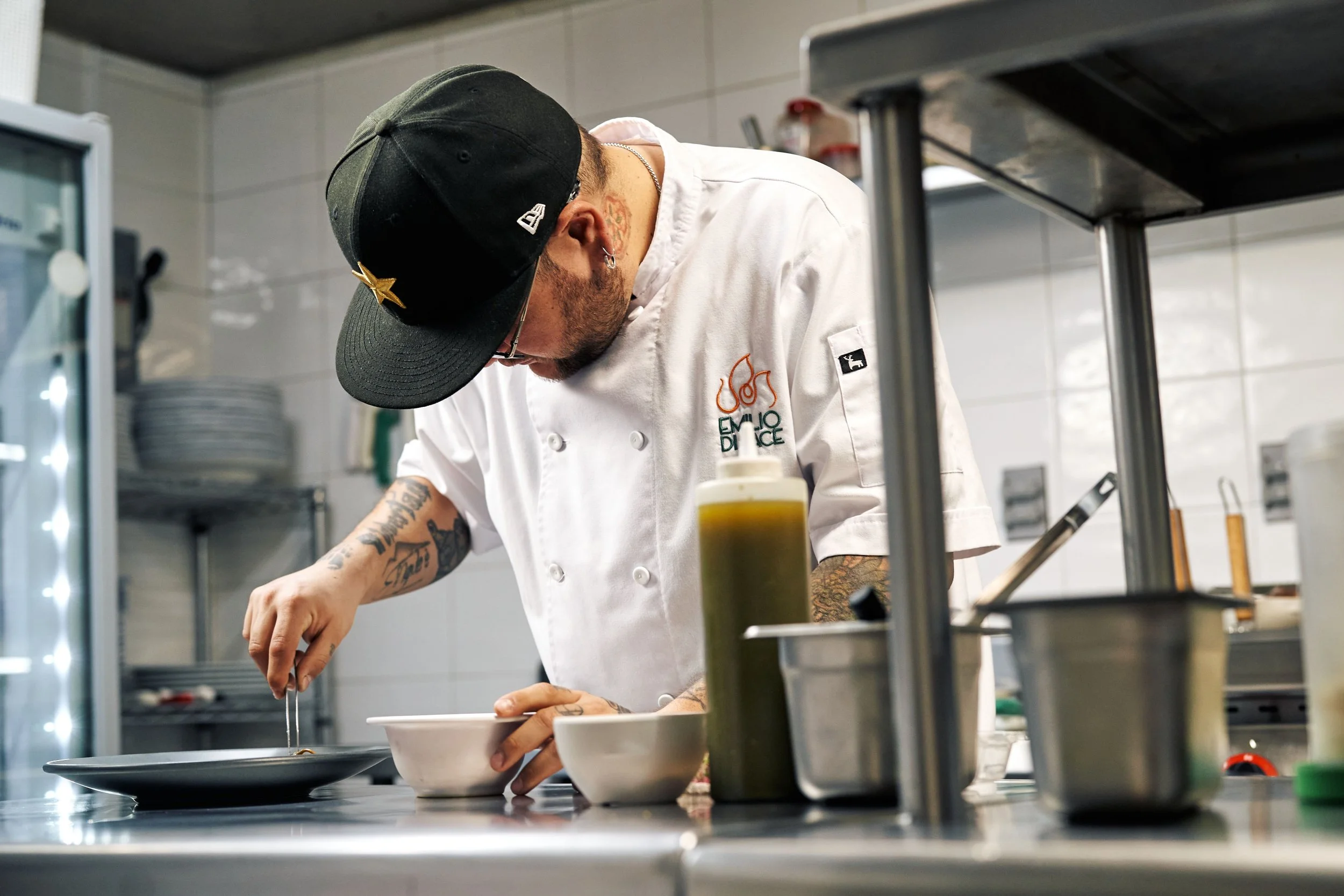 Chef in a white uniform and black cap preparing food in a commercial kitchen.