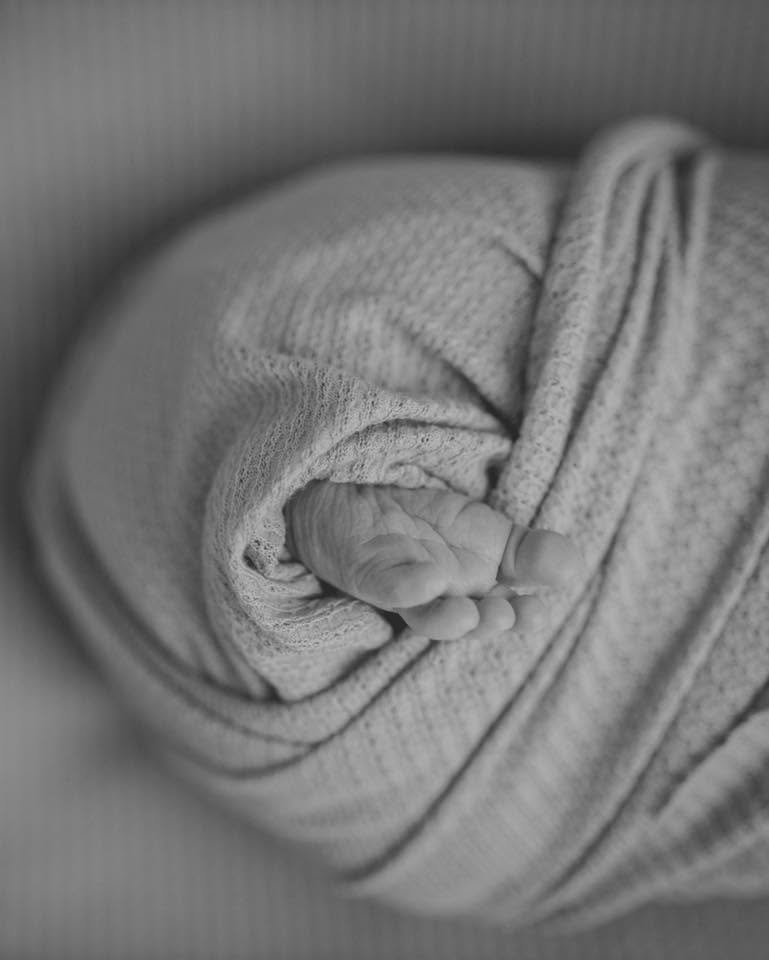 Close-up of a tiny baby sock wrapped around a newborn baby's foot, black and white photo.
