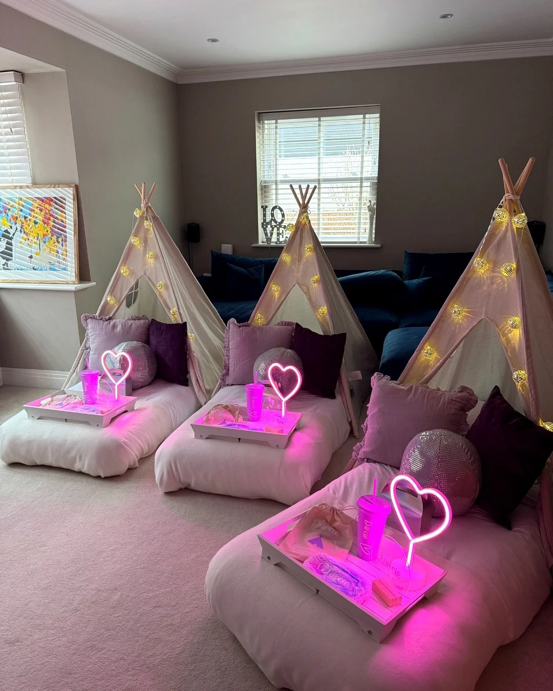 Pink teepee sleepover party setup with personalised trays, heart lights, fairy lights and cosy bedding