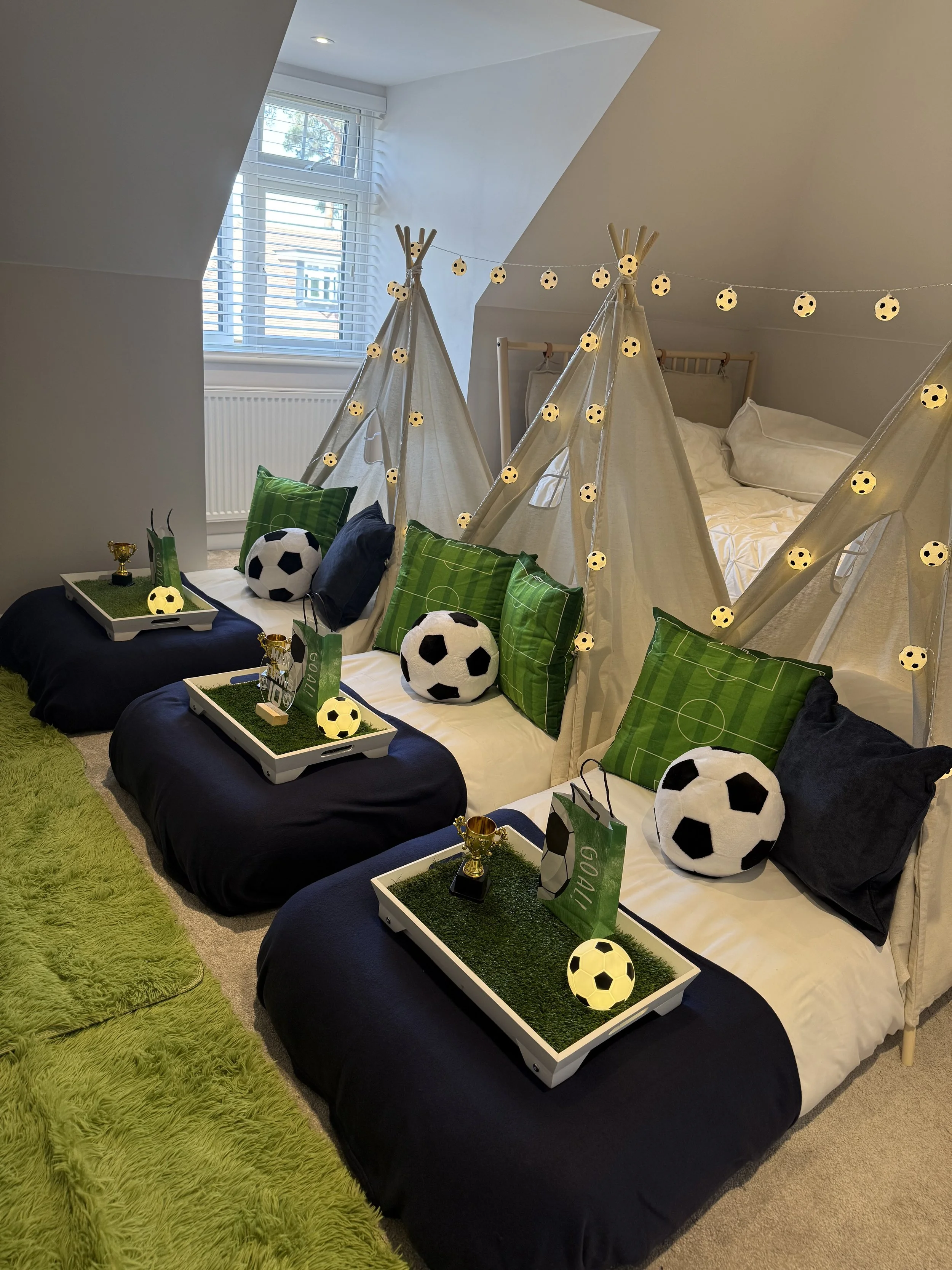 Three teepees styled for a football sleepover party with football cushions, green pitch trays and glowing star lights