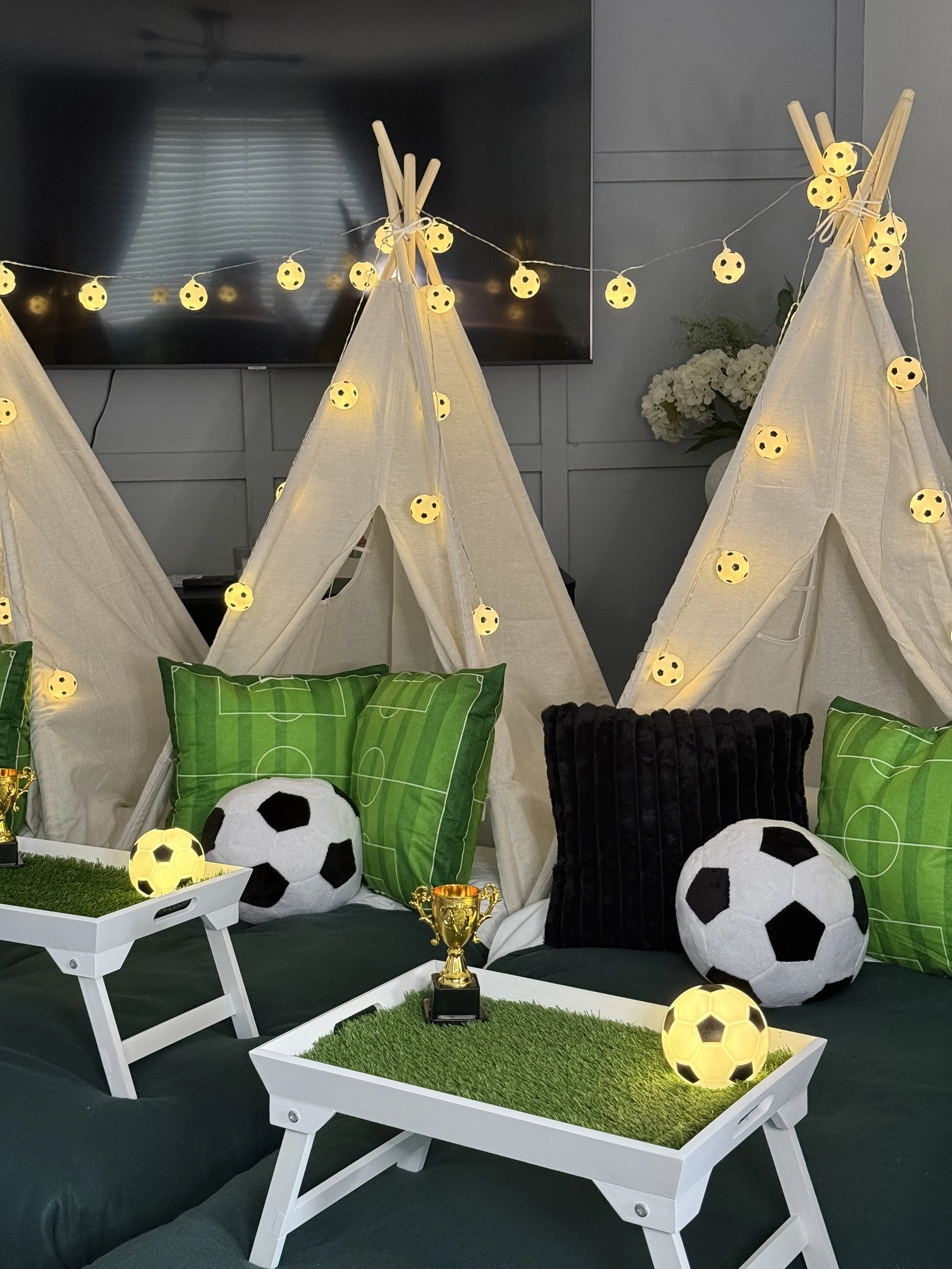Match Day Magic teepee sleepover party by Sweet Dreams Events in the evening showing three cream teepees with glowing football fairy lights and grass effect trays styled for a boys birthday party in Surrey