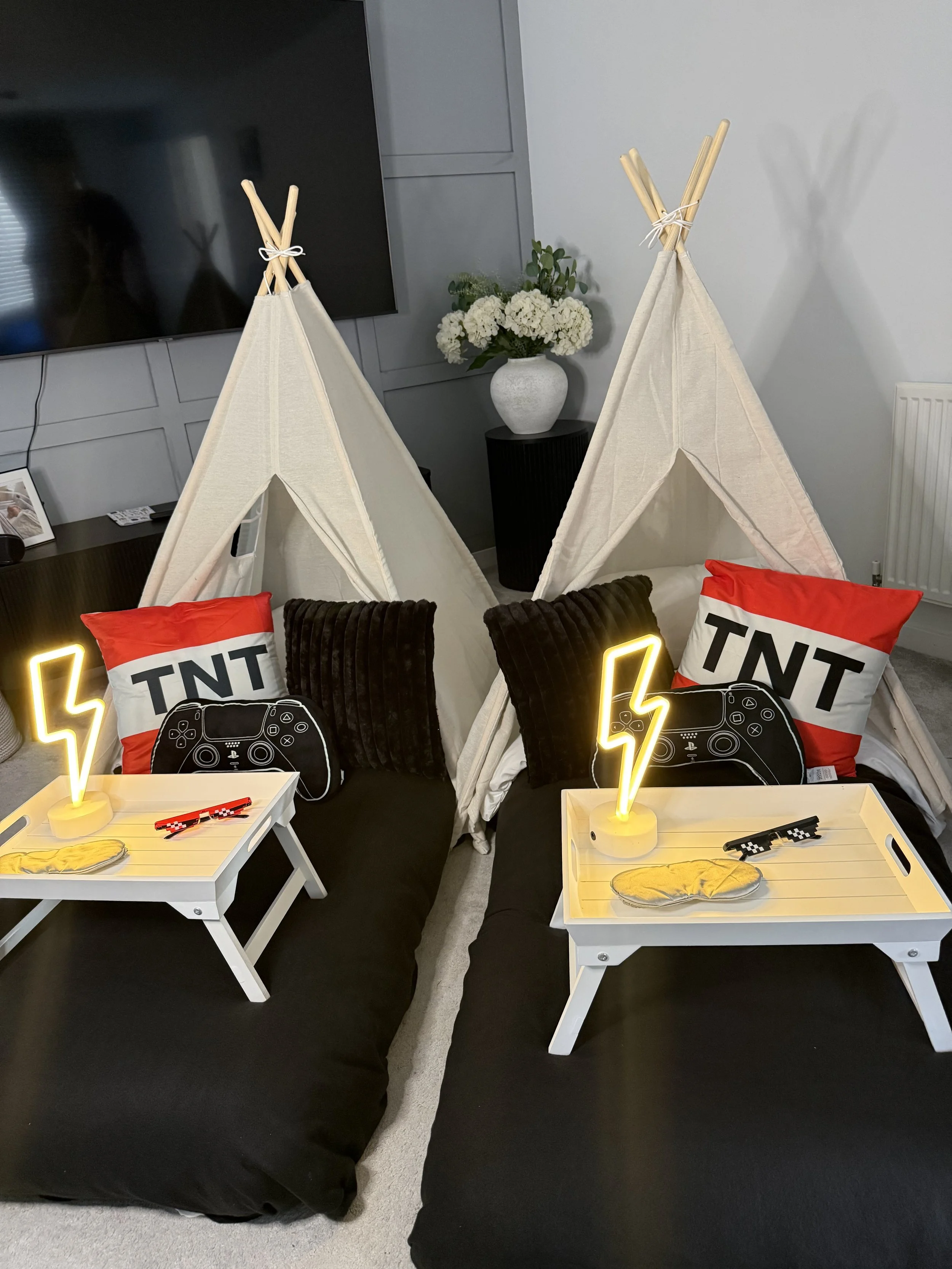Level Up Lair gaming teepee sleepover with two cream teepees, TNT cushions, games controller cushions, glowing neon bolts and trays with pixel sunglasses and sleep masks