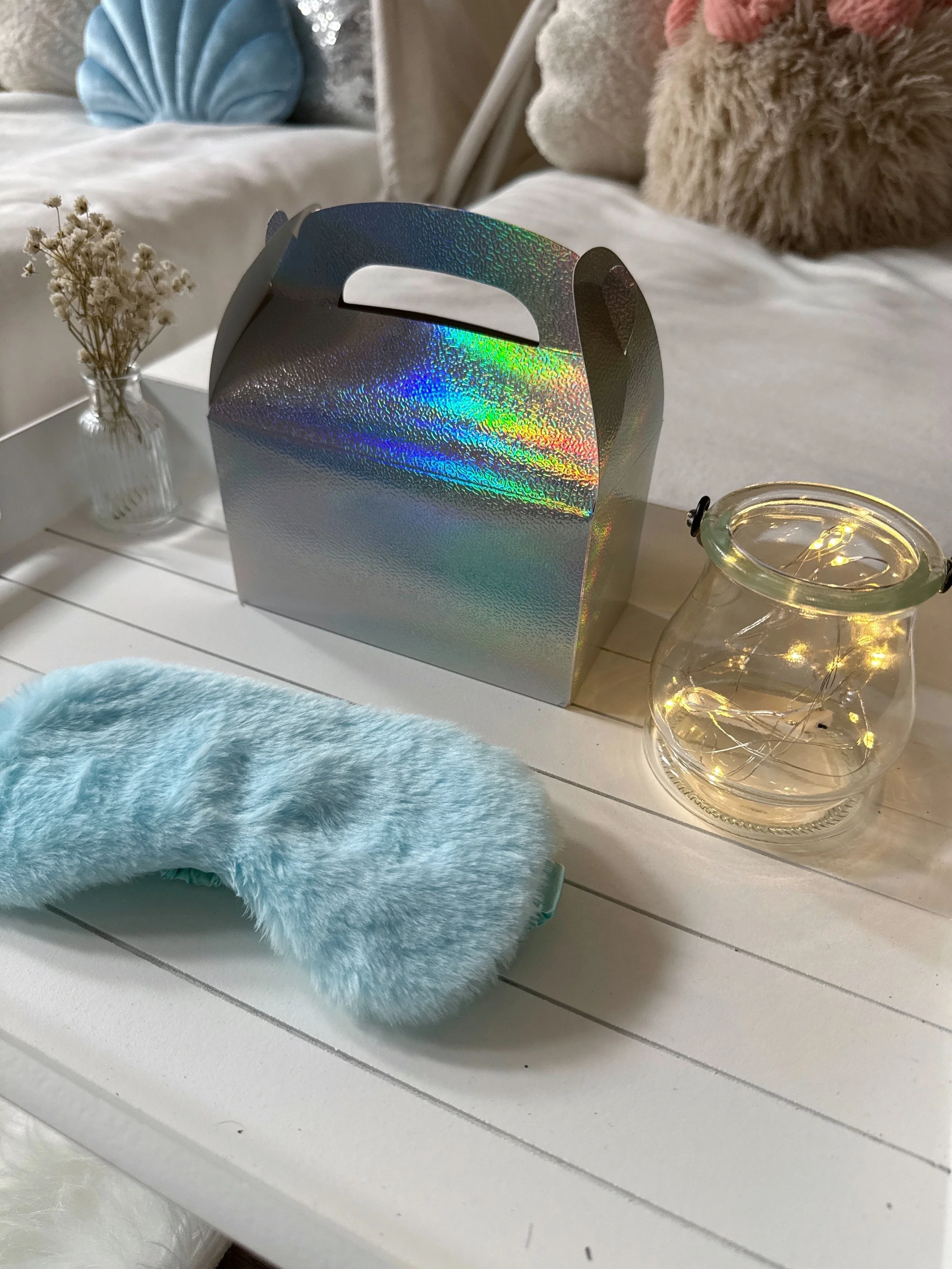 Personalised sleepover tray with holographic treat box, blue sleep mask, and fairy light jar from a Mermaid Lagoon party.
