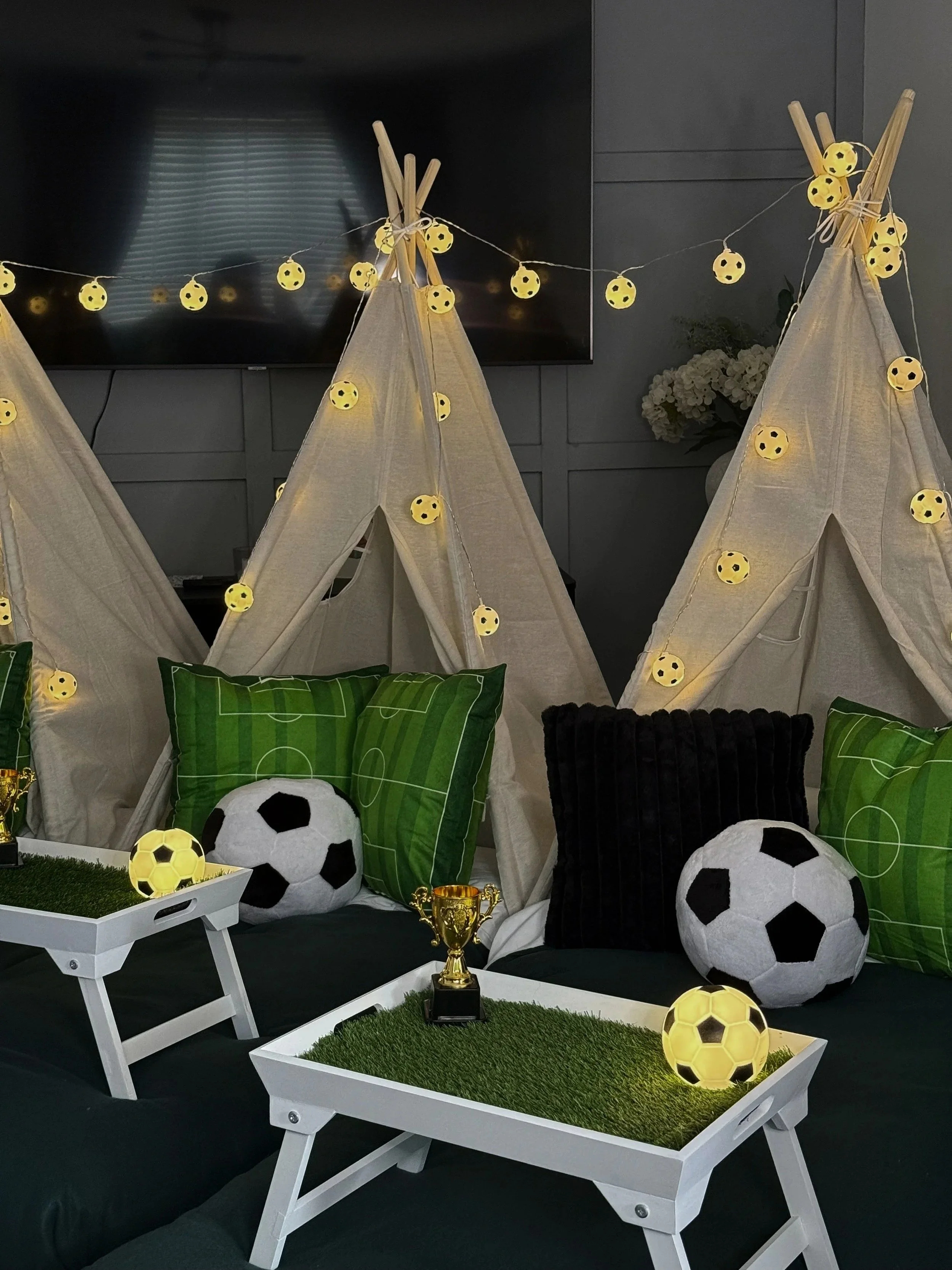 Match Day Magic teepee sleepover party by Sweet Dreams Events showing cream teepees with football fairy lights, green pitch cushions, football soft toys and gold trophy props styled for a childs football birthday party in Surrey