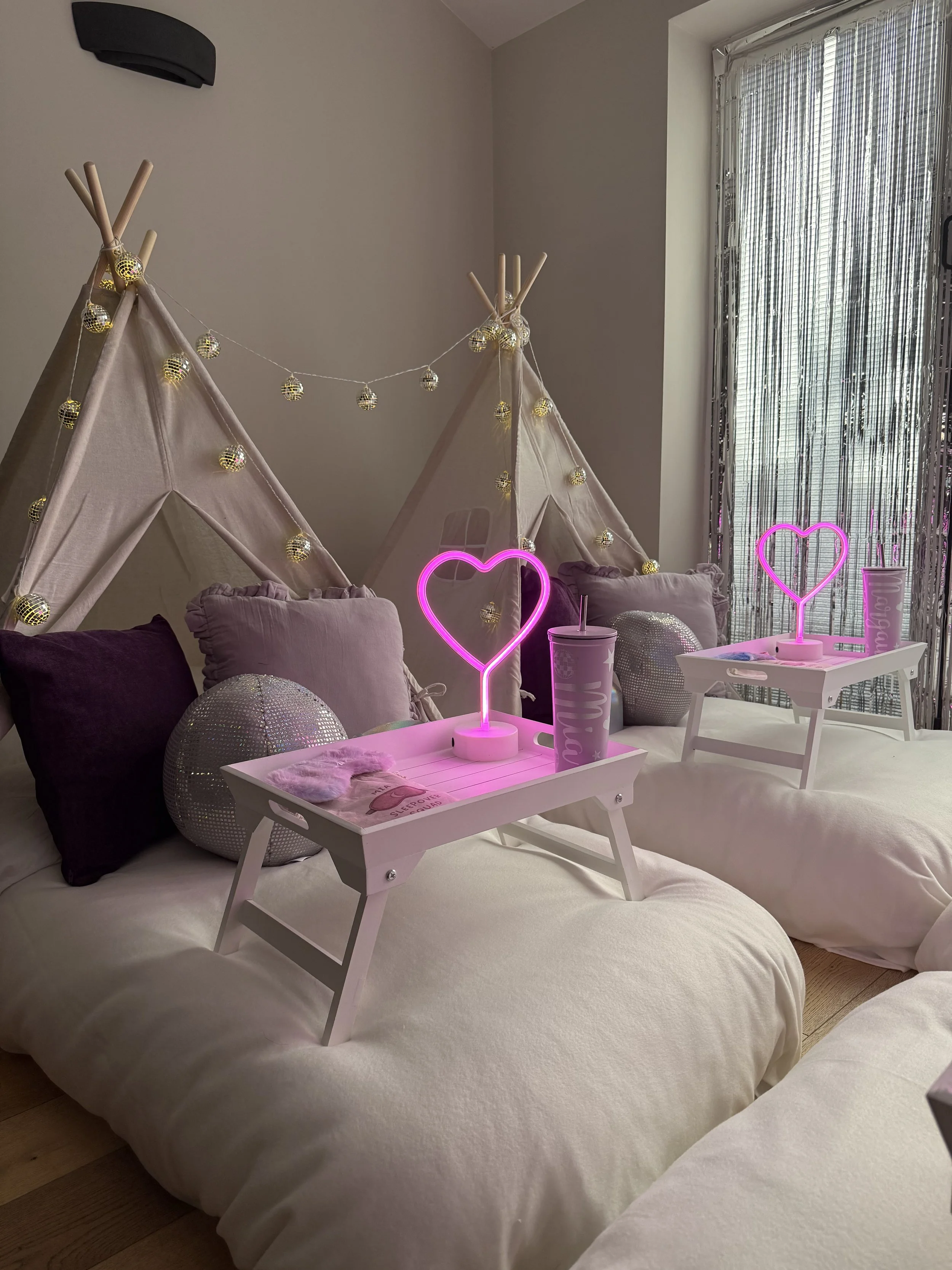 Glitterball Disco Dreams teepee sleepover party by Sweet Dreams Events, showing white breakfast trays with neon heart lamps, personalised cups, sleep masks, disco ball props and silver sequin cushions, styled for a girls sleepover party in Sussex