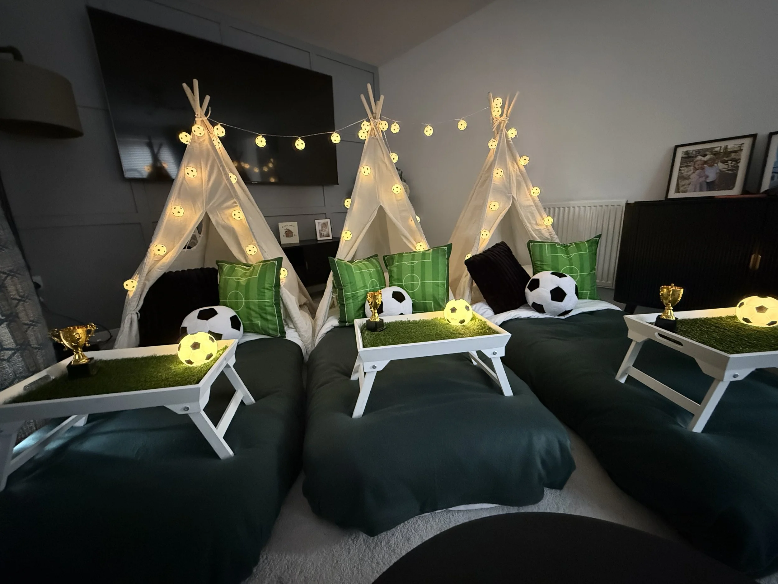 Match Day Magic football teepee sleepover party setup by Sweet Dreams Events in Surrey, with three white teepees, green football pitch cushions, astroturf serving trays, glowing football lights and gold trophy decorations