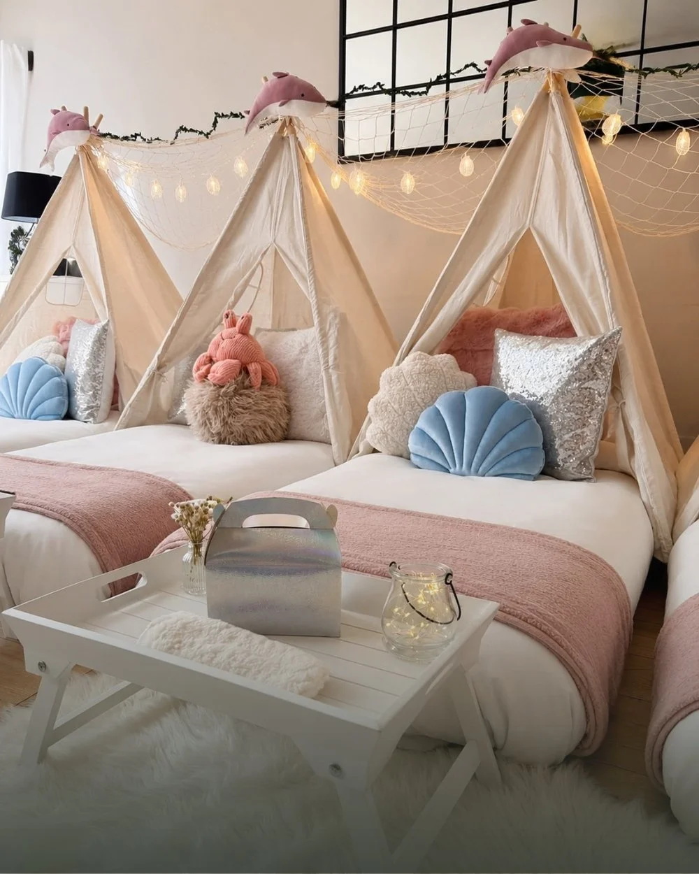 Three teepees styled for a mermaid sleepover with shell cushions, dolphin toppers and fairy lit netting