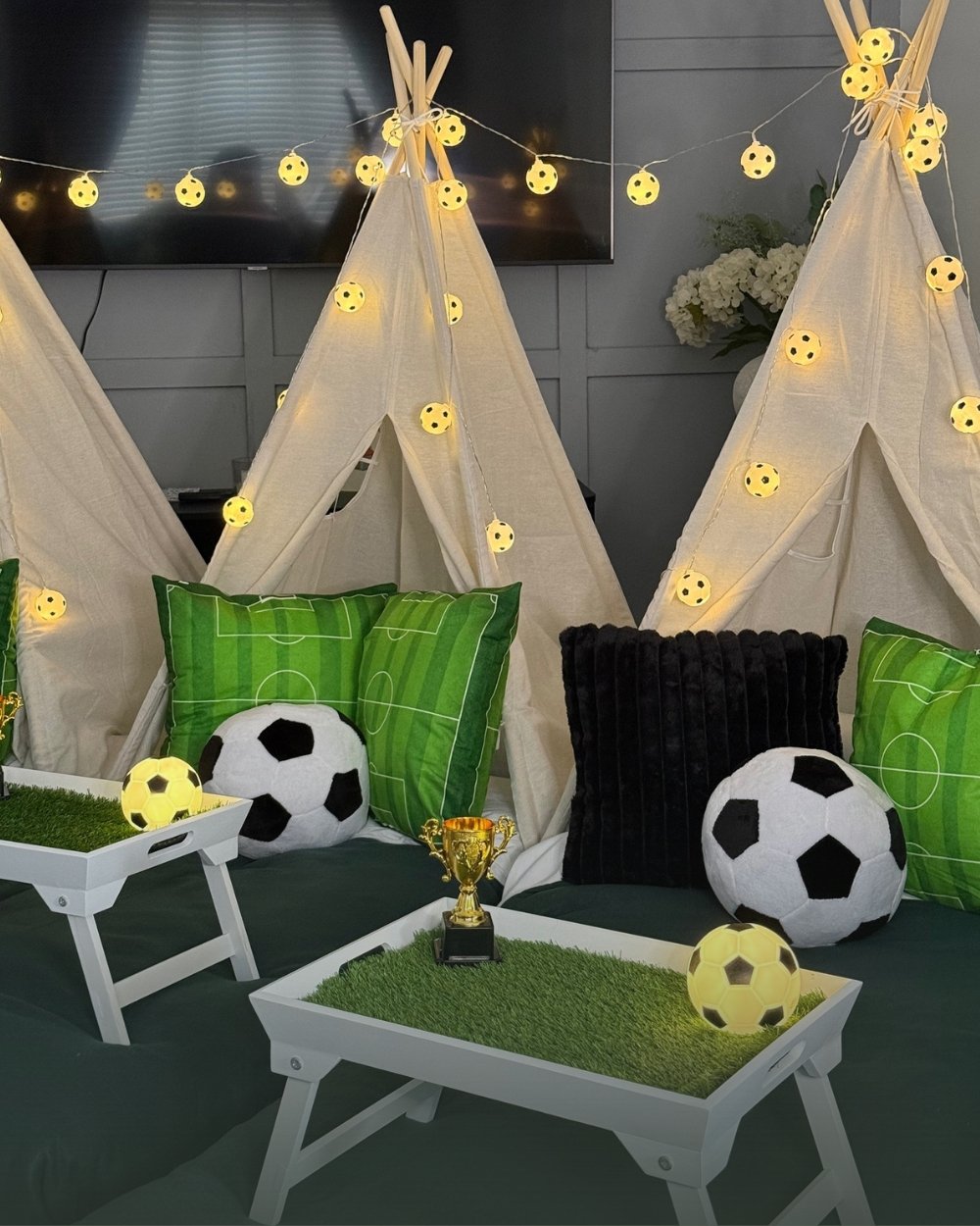 Teepees styled for a football themed sleepover with pitch cushions, footballs and a gold trophy