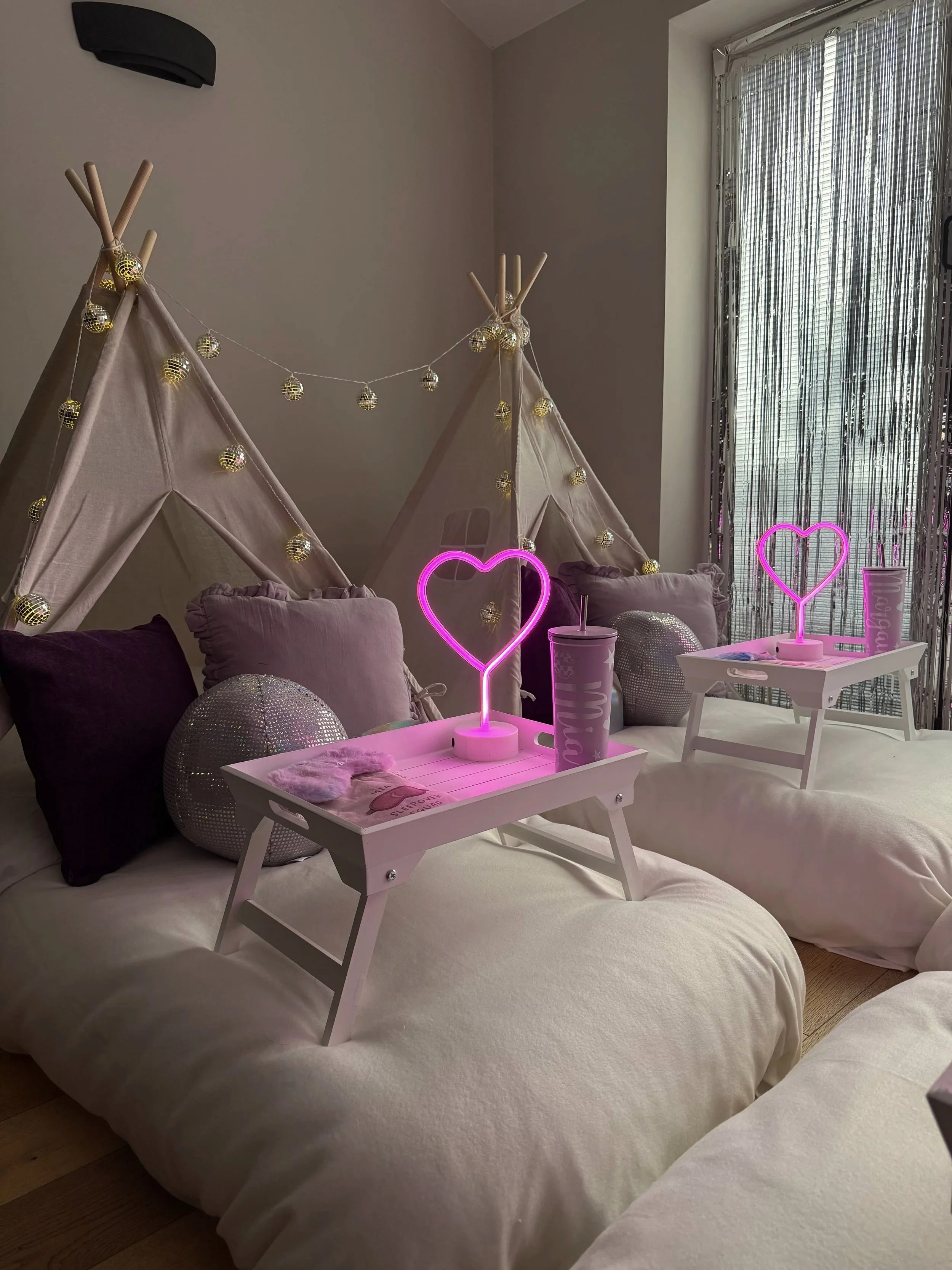 Glitterball Disco Dreams teepee sleepover party by Sweet Dreams Events, showing white breakfast trays with neon heart lamps, personalised cups, sleep masks, disco ball props and silver sequin cushions, styled for a girls sleepover party in Sussex