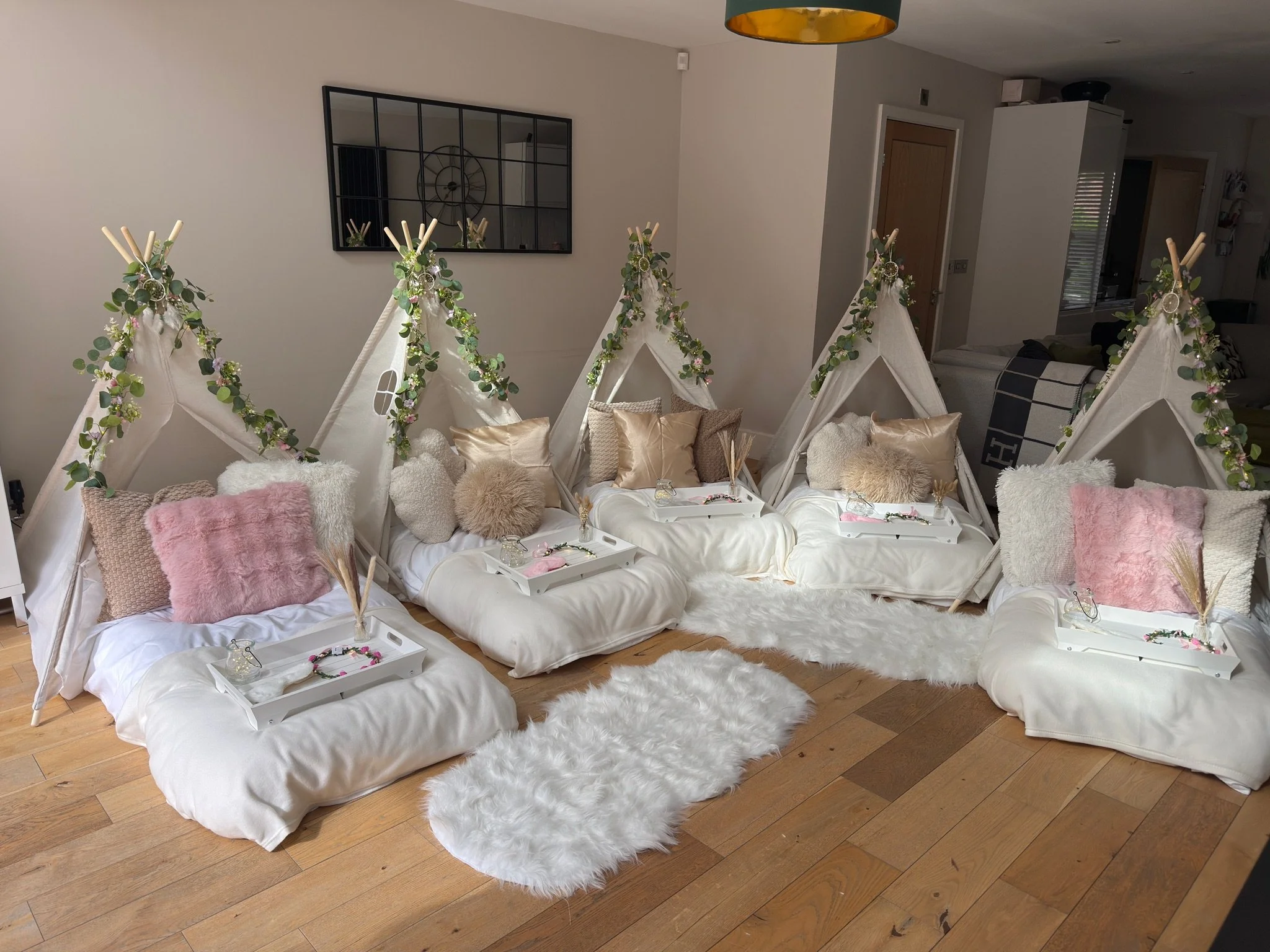 Boho chic teepee sleepover party setup by Sweet Dreams Events in Surrey, featuring white canvas teepees with eucalyptus garlands, blush pink cushions, fluffy throws and white serving trays