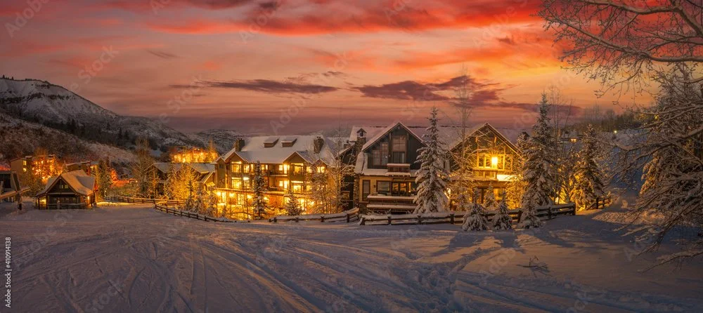 Snowy village houses illuminated at dusk with orange and pink sky
