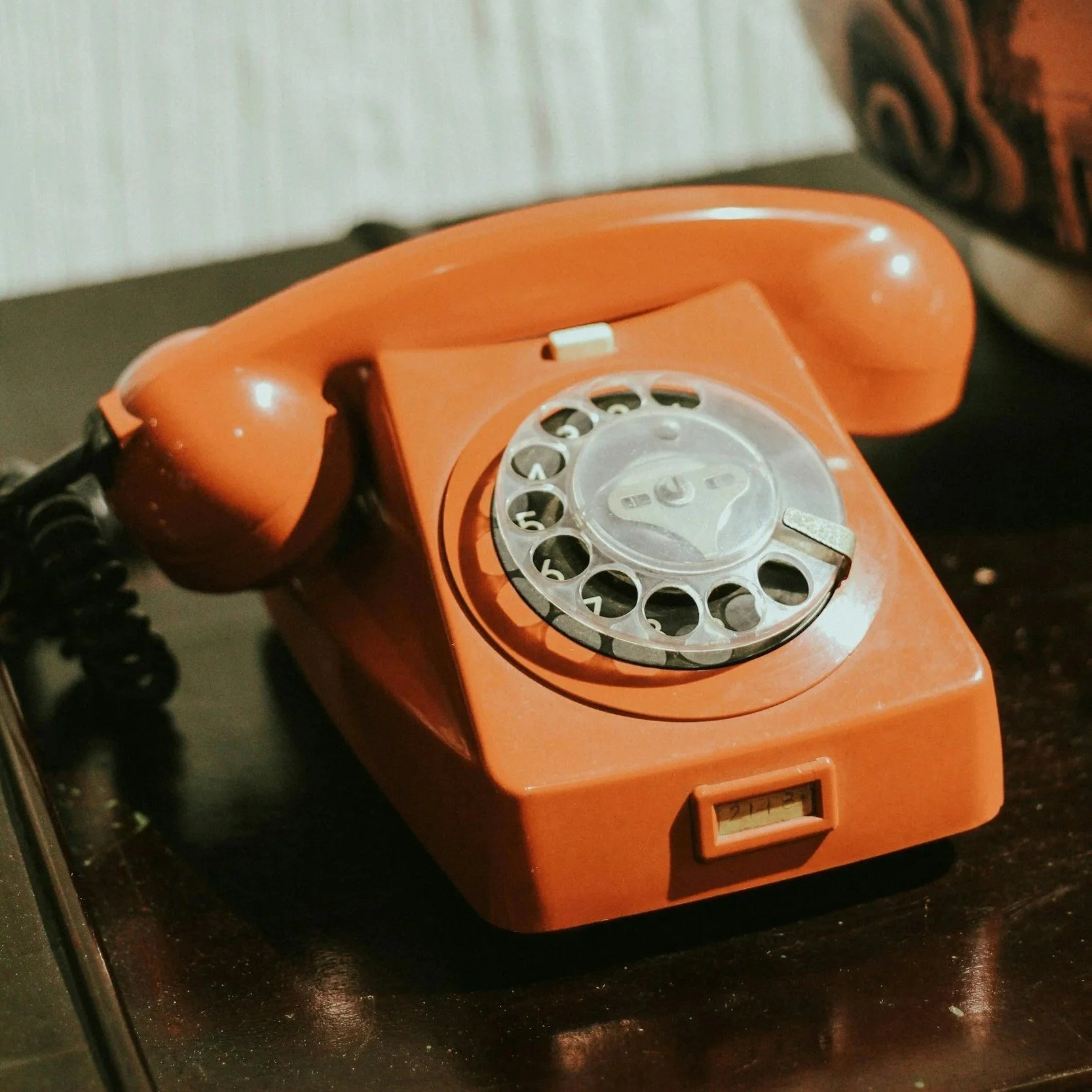 An orange vintage rotary phone resting on a dark surface.