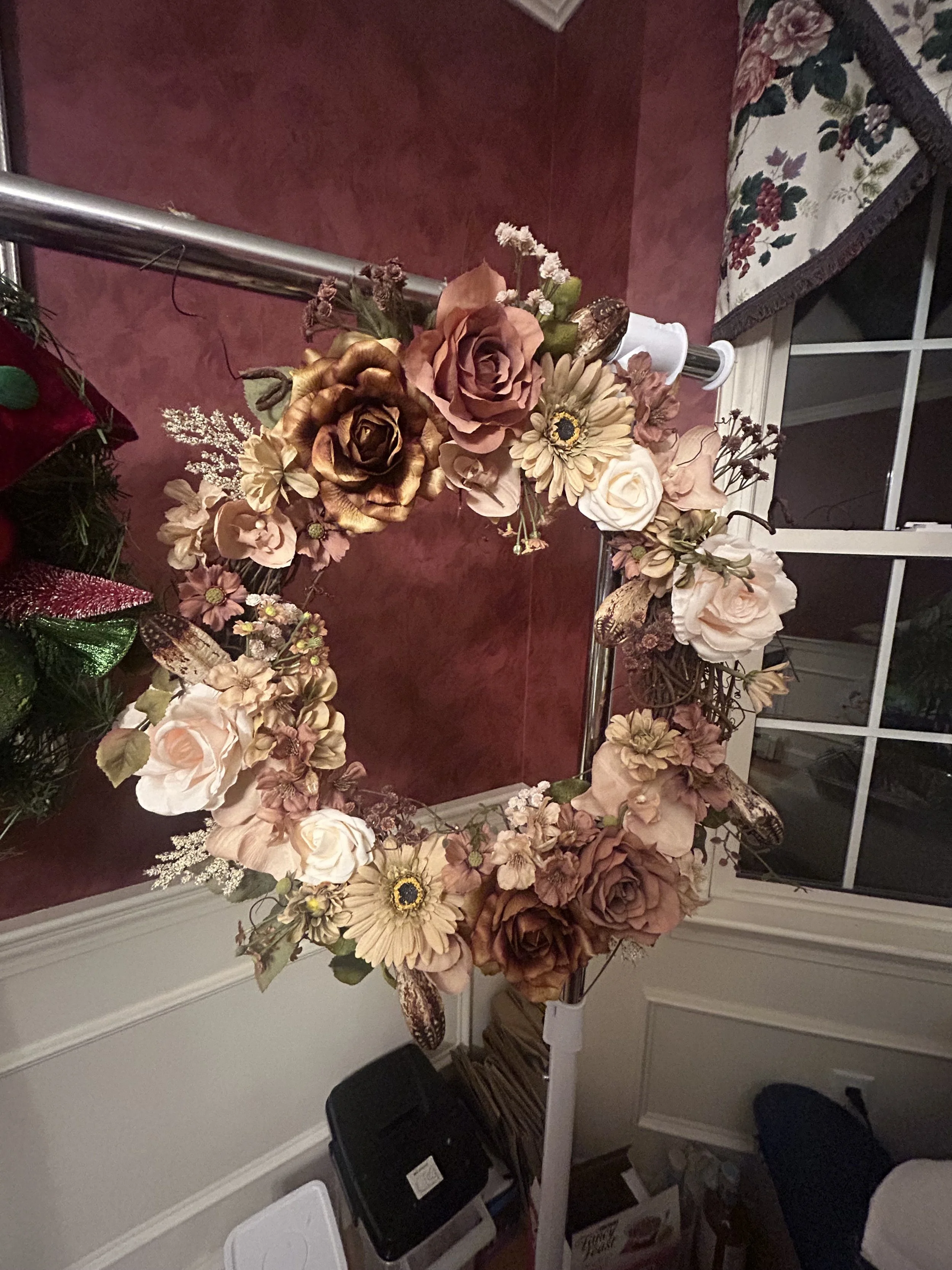 Artificial floral arrangement on a table near a window, featuring pink, beige, and brown flowers and foliage.