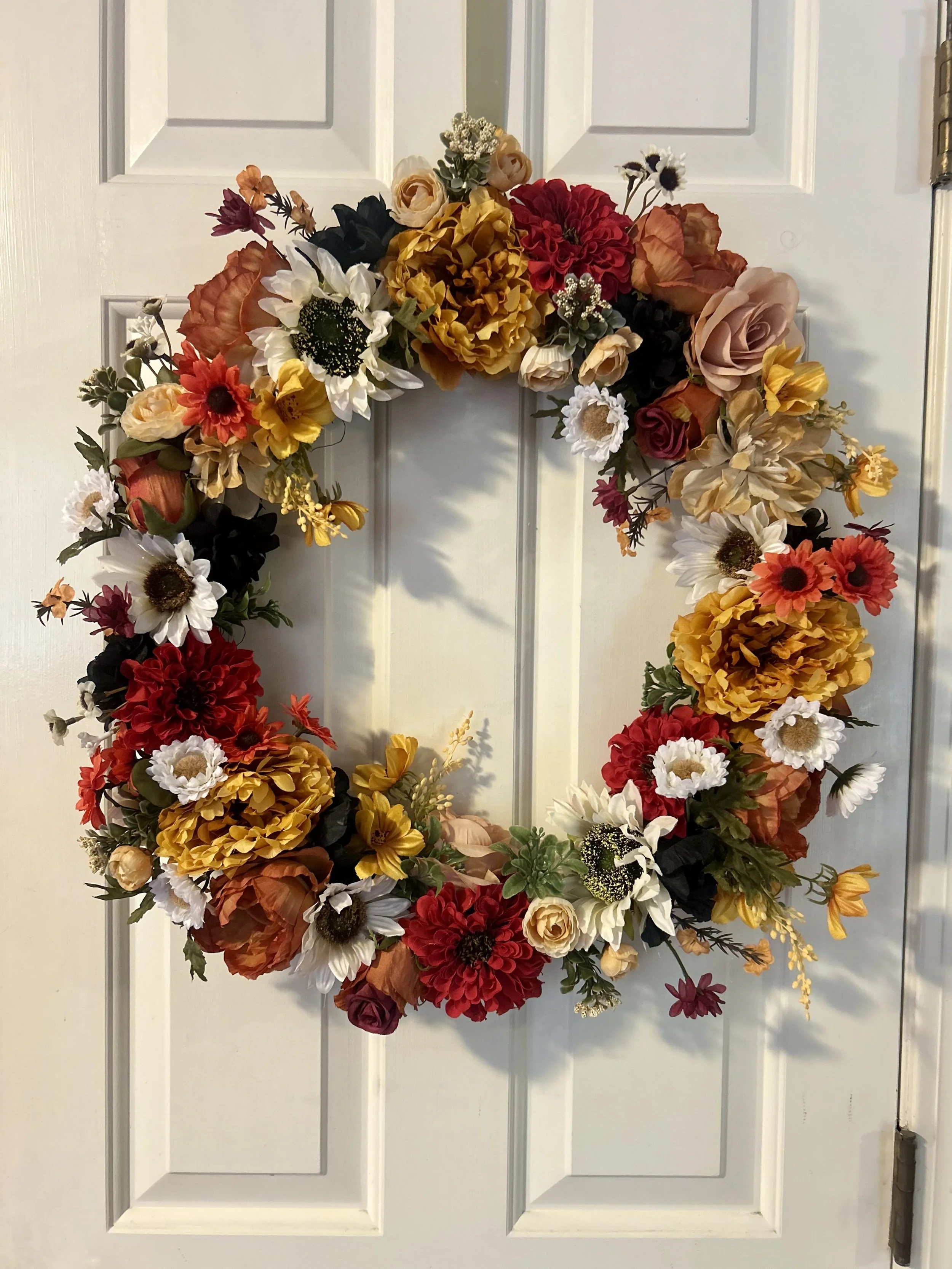 A decorative floral wreath hanging on a white door with four rectangular panels.