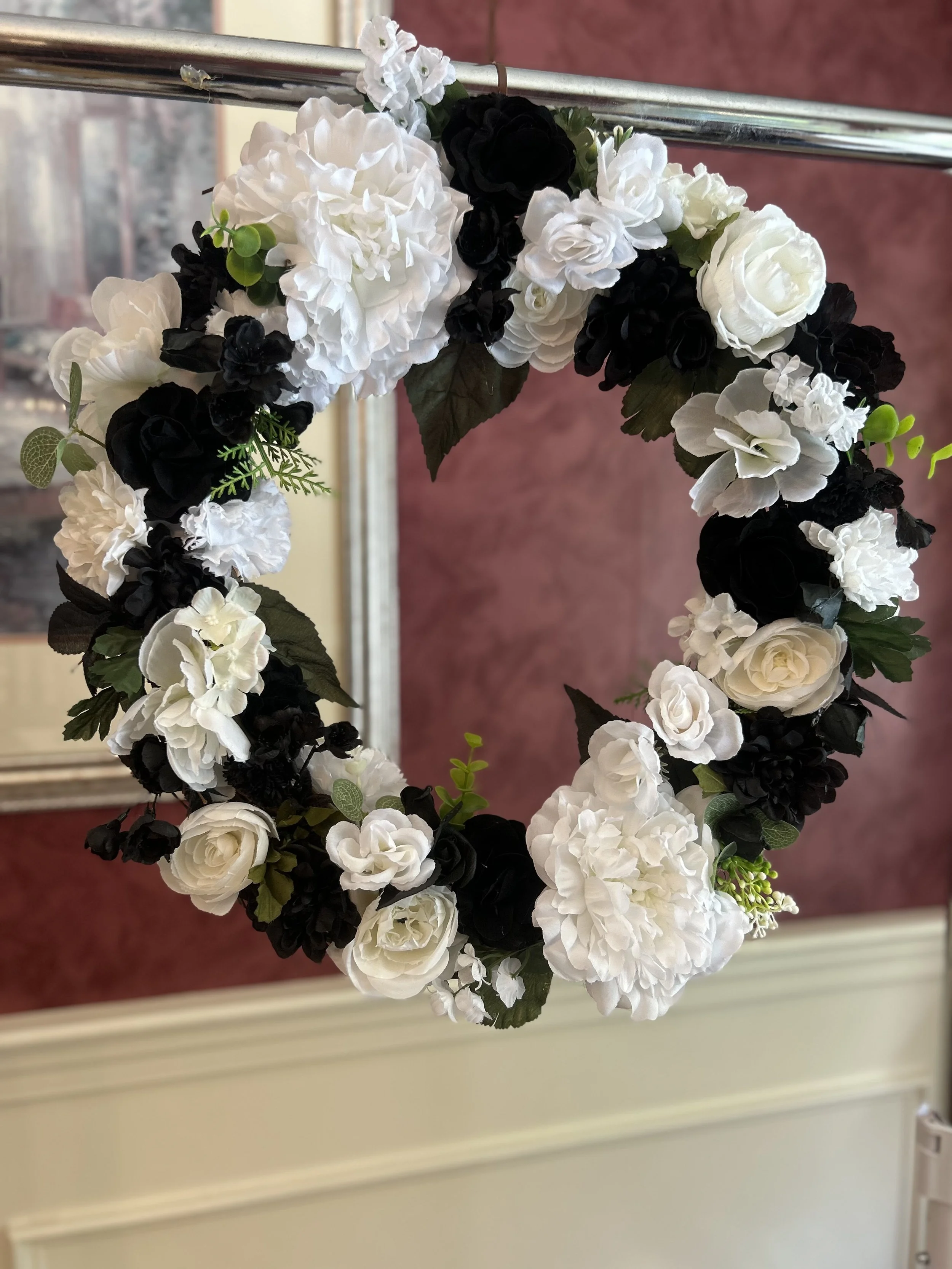 A floral crown made of white and black artificial flowers hanging on a metal rail.