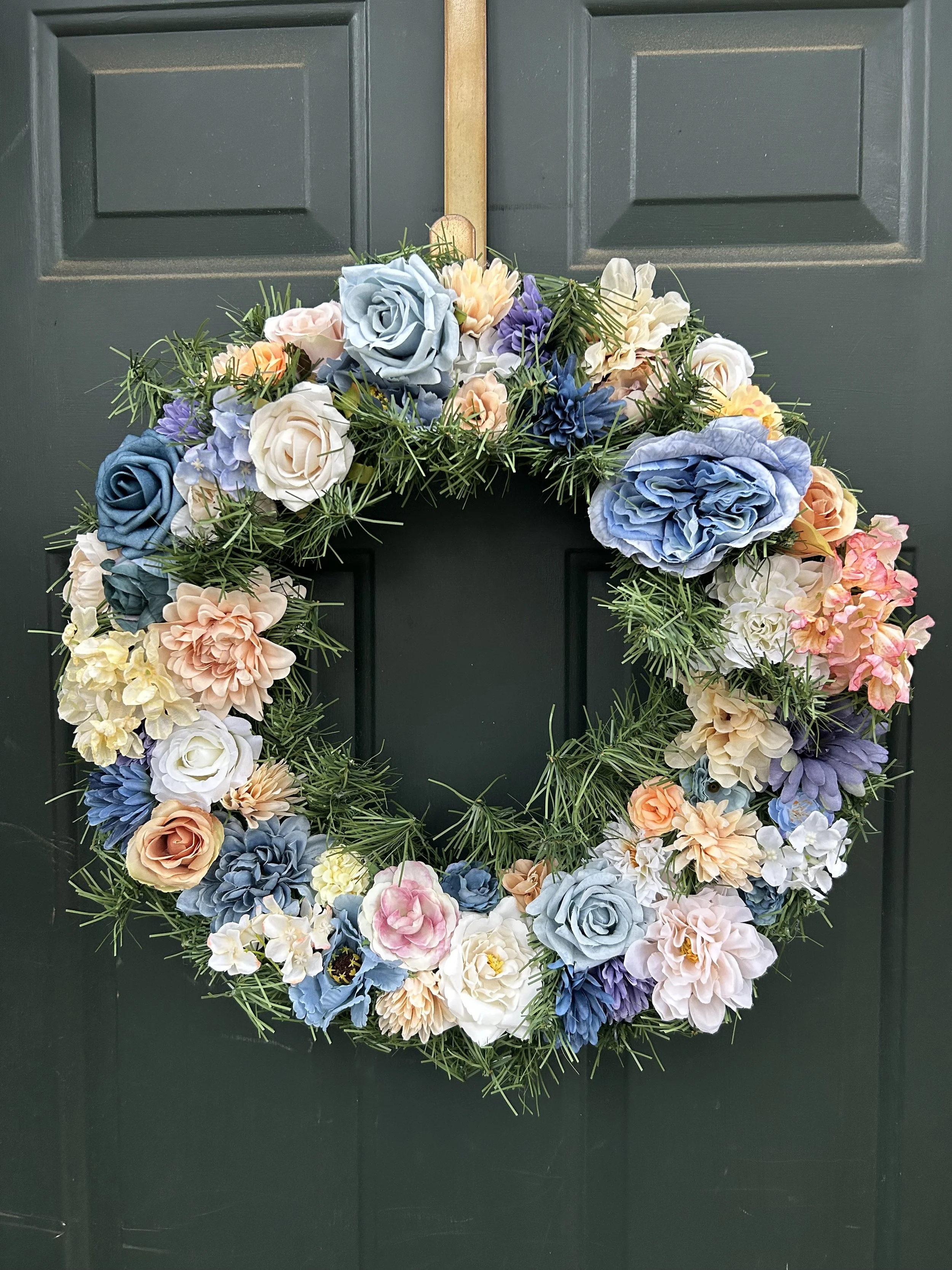 A floral wreath with various colored flowers hanging on a dark green door.