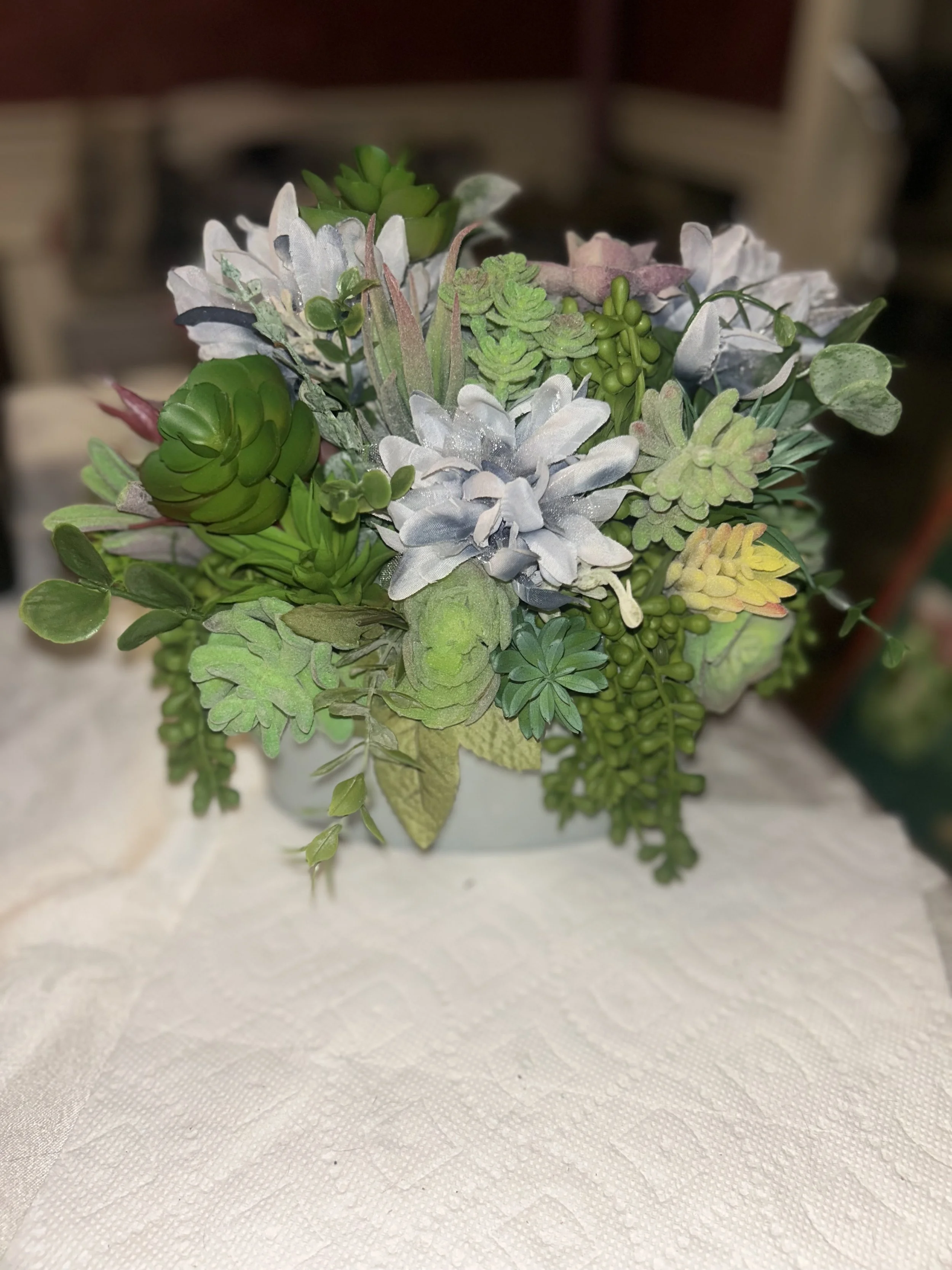 Artificial bouquet of succulents and green leaves on a textured white surface.