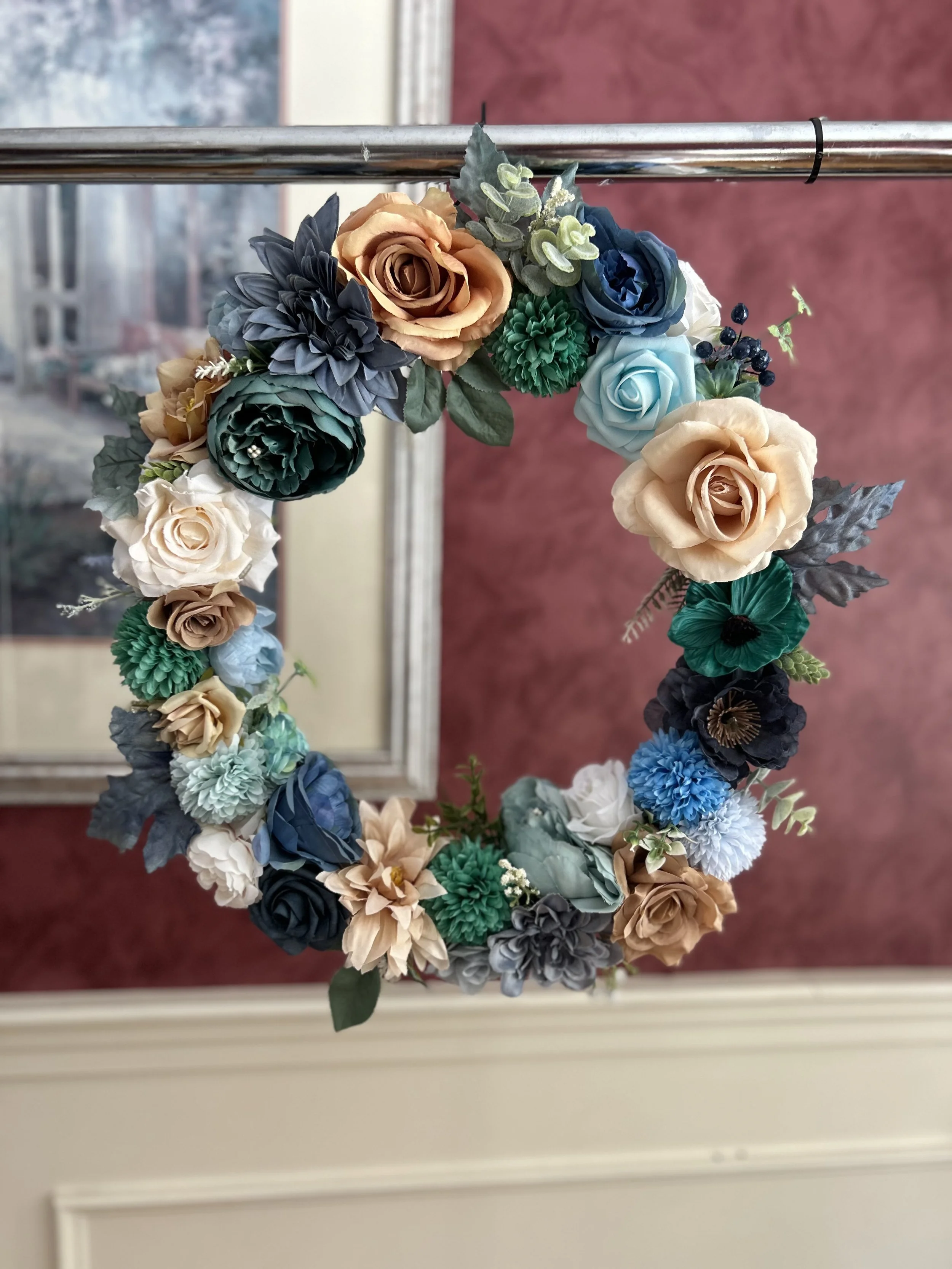A floral wreath with peach, blue, green, and cream-colored roses and greenery hanging on a door or mirror.