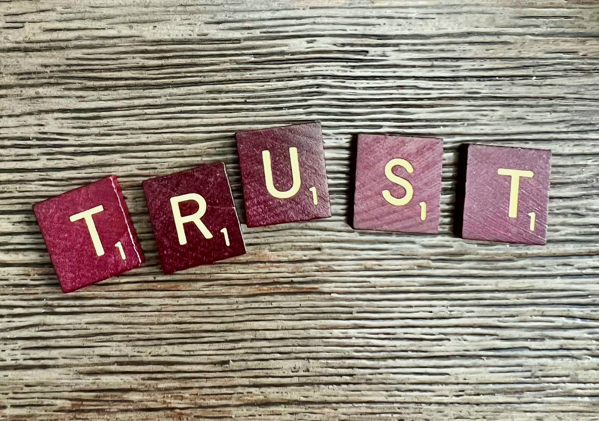 Scrabble tiles spelling the word "TRUST" on a wooden surface.