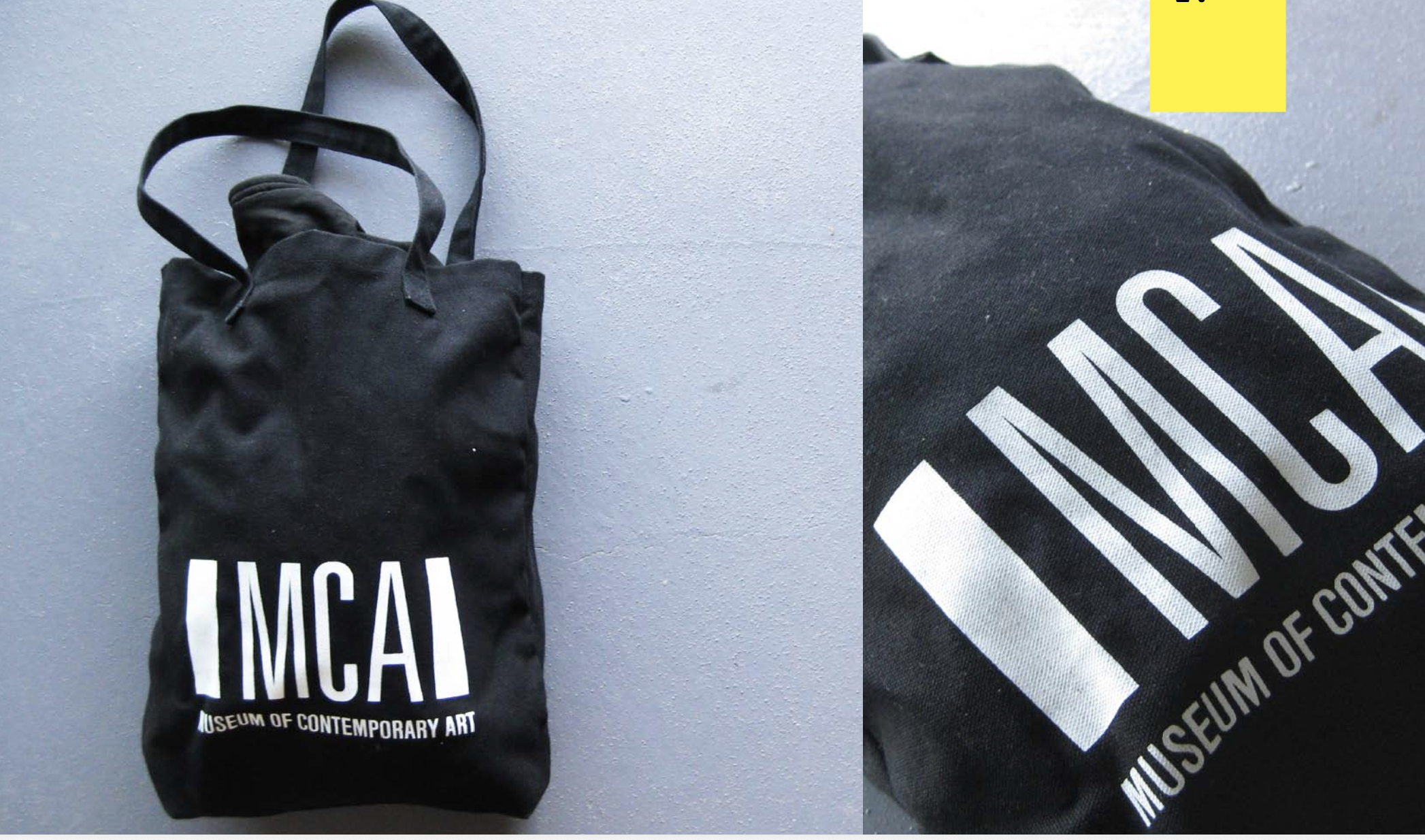 Black tote bag with white text reading "MUSEUM OF CONTEMPORARY ART" on a gray surface, shown from front and close-up.