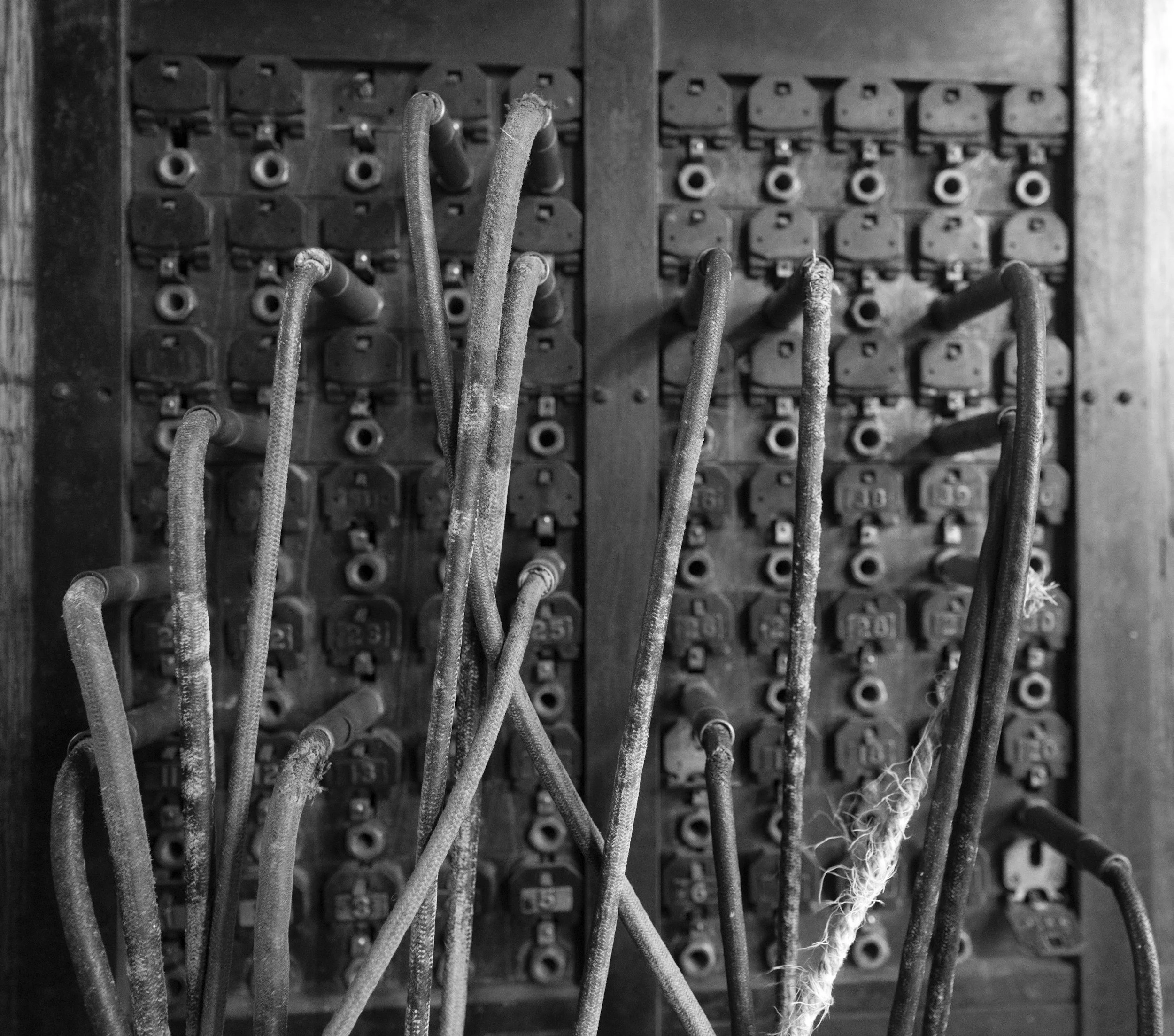 Black and white photo of an old electrical panel with several frayed, dusty wires protruding from it.