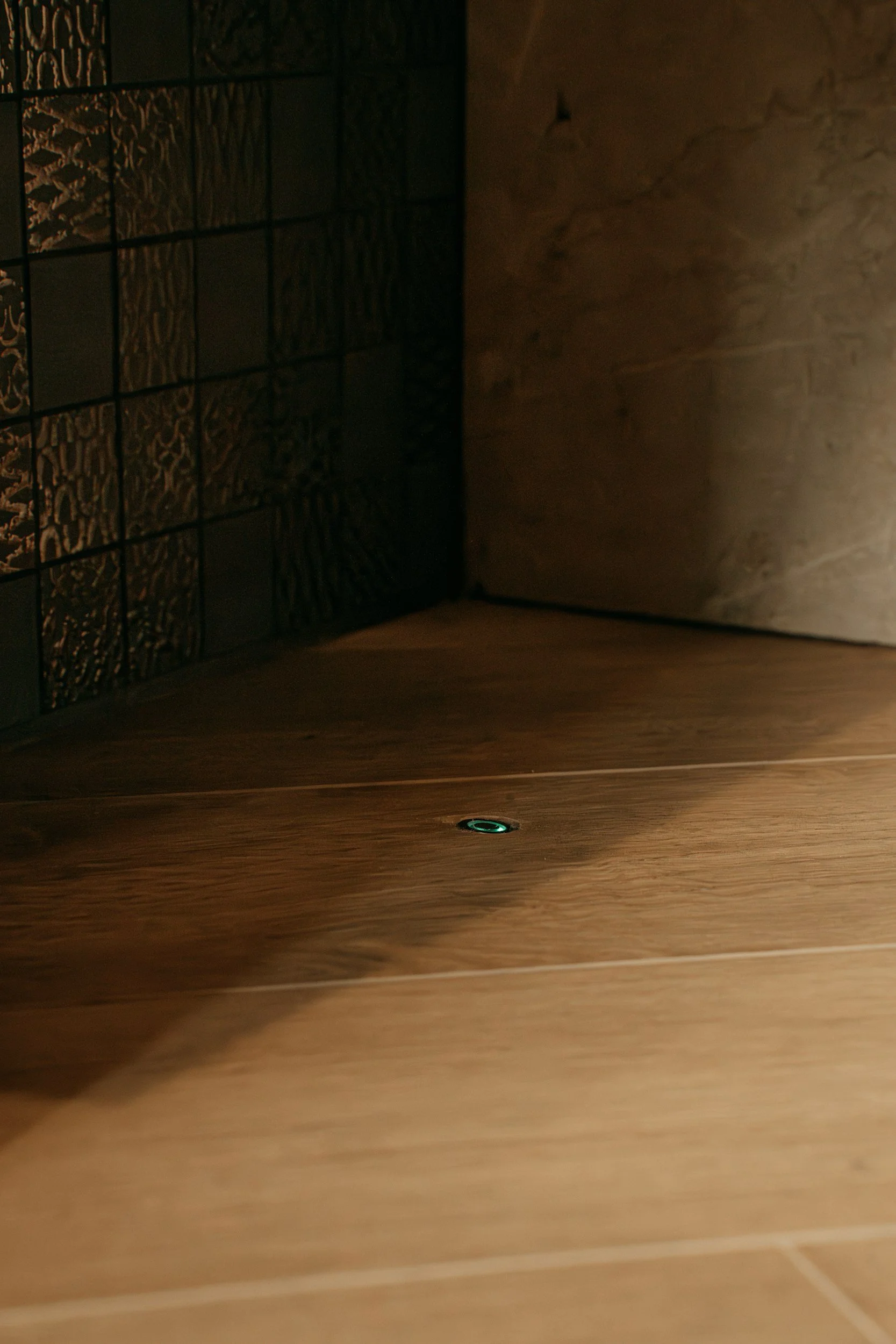 Close-up of a wooden surface with a small illuminated circular element in the middle, with a textured wall and decorative screen to the left.